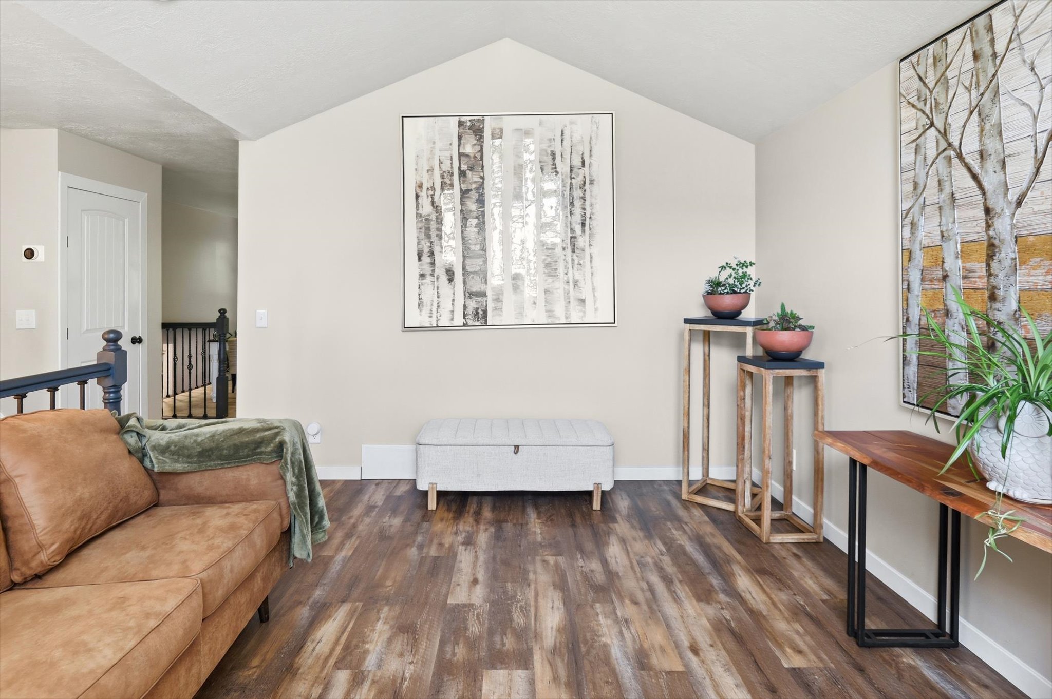 Vaulted ceiling with recessed lighting, wood-finish flooring, light neutral wall paint, white trim, and a white interior door