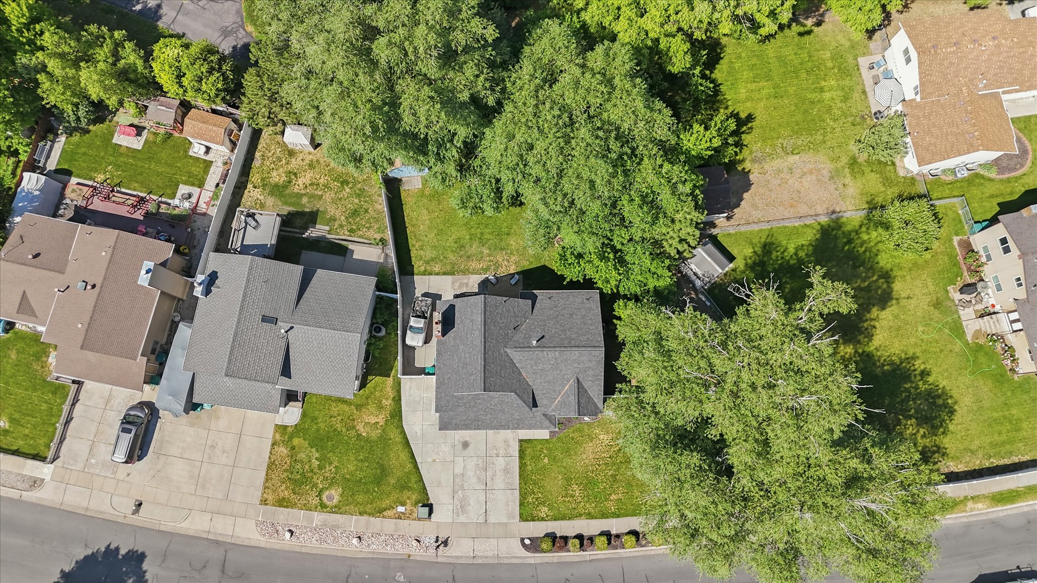 Aerial perspective showcasing a property with a gray shingled roof, a paved driveway, and surrounding green spaces