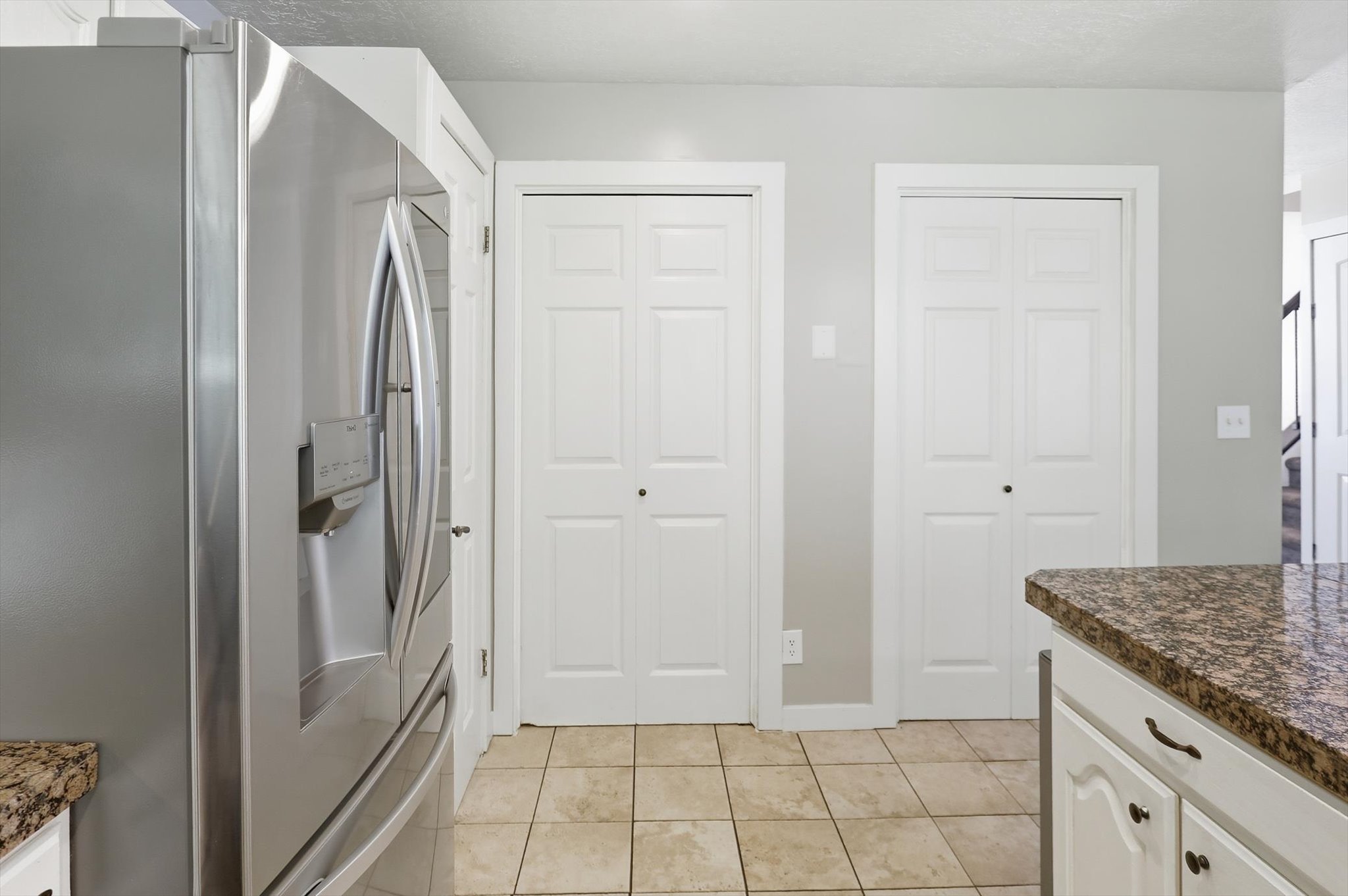 Kitchen featuring stainless steel refrigerator, patterned tile flooring, and white bi-fold doors