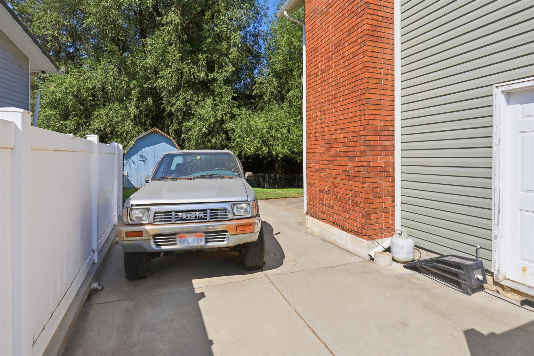 Concrete driveway extending alongside the structure, featuring a white vinyl privacy fence and a red brick exterior accent
