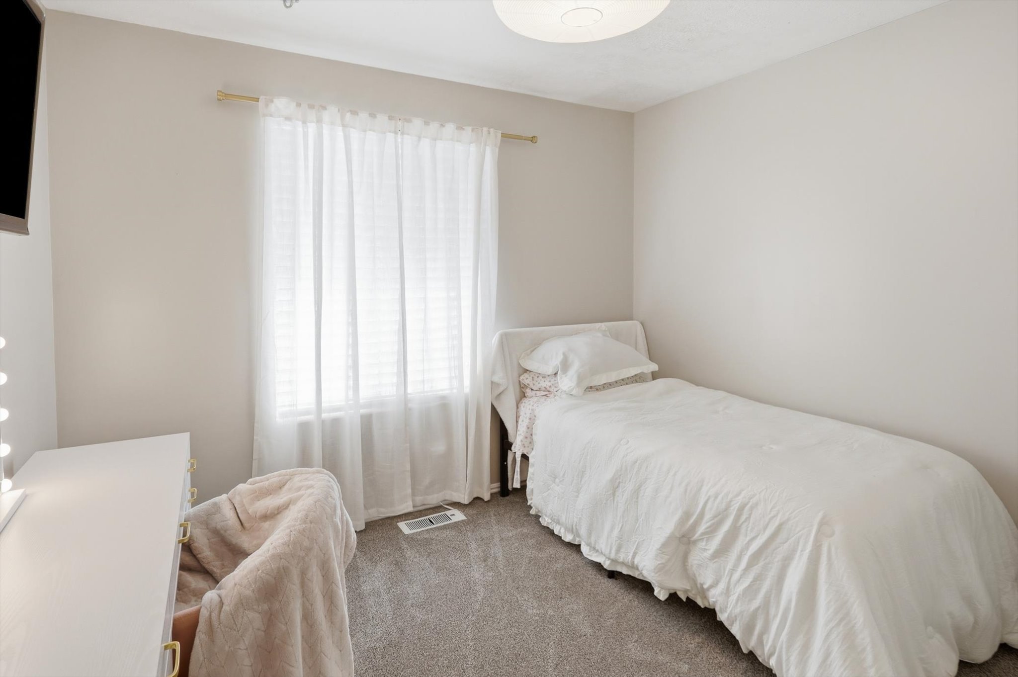 Carpeted room with a large window, a ceiling-mounted light fixture, and neutral-toned walls