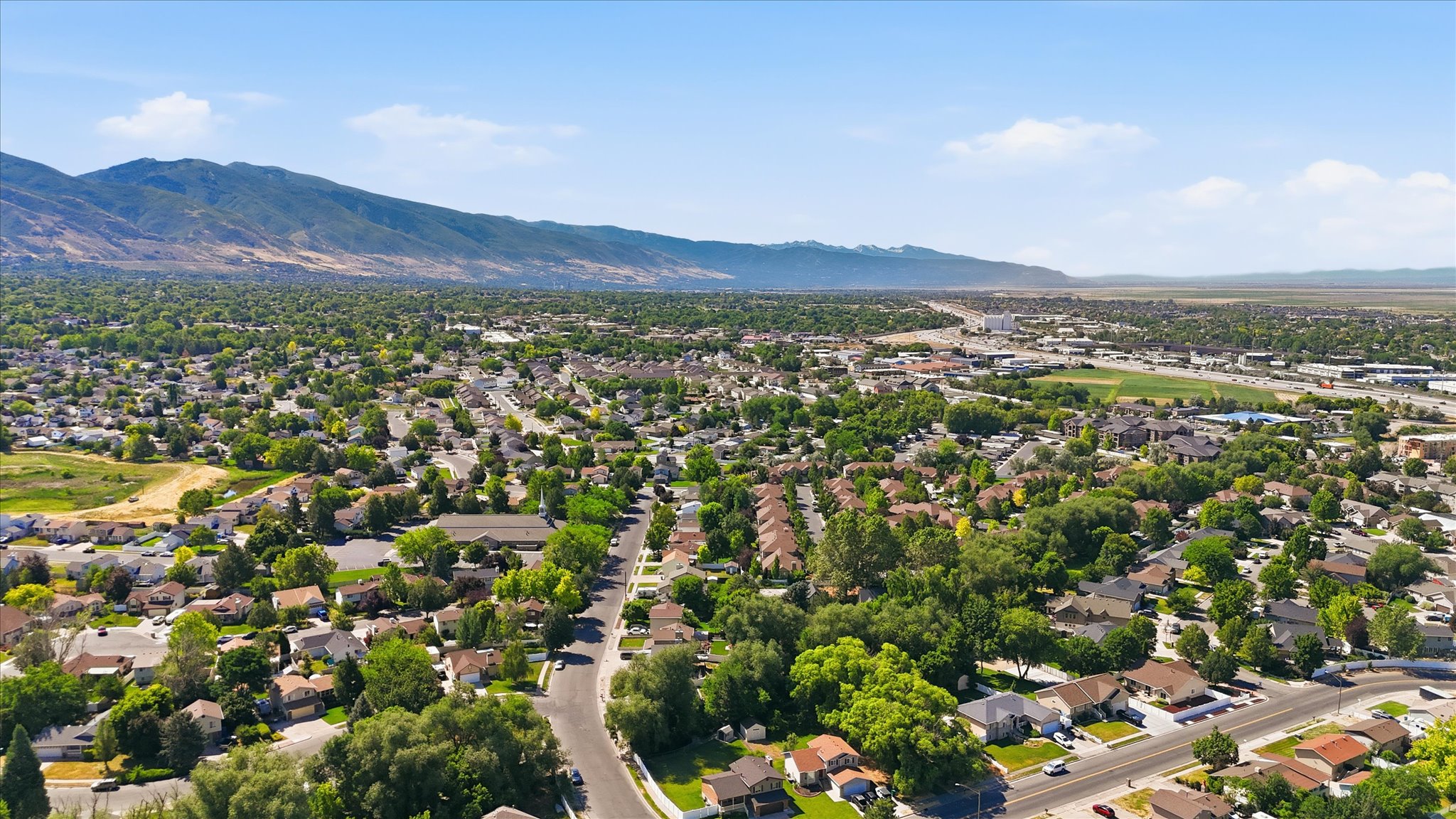 Expansive aerial showcasing a residential area with mature tree cover and mountain backdrops