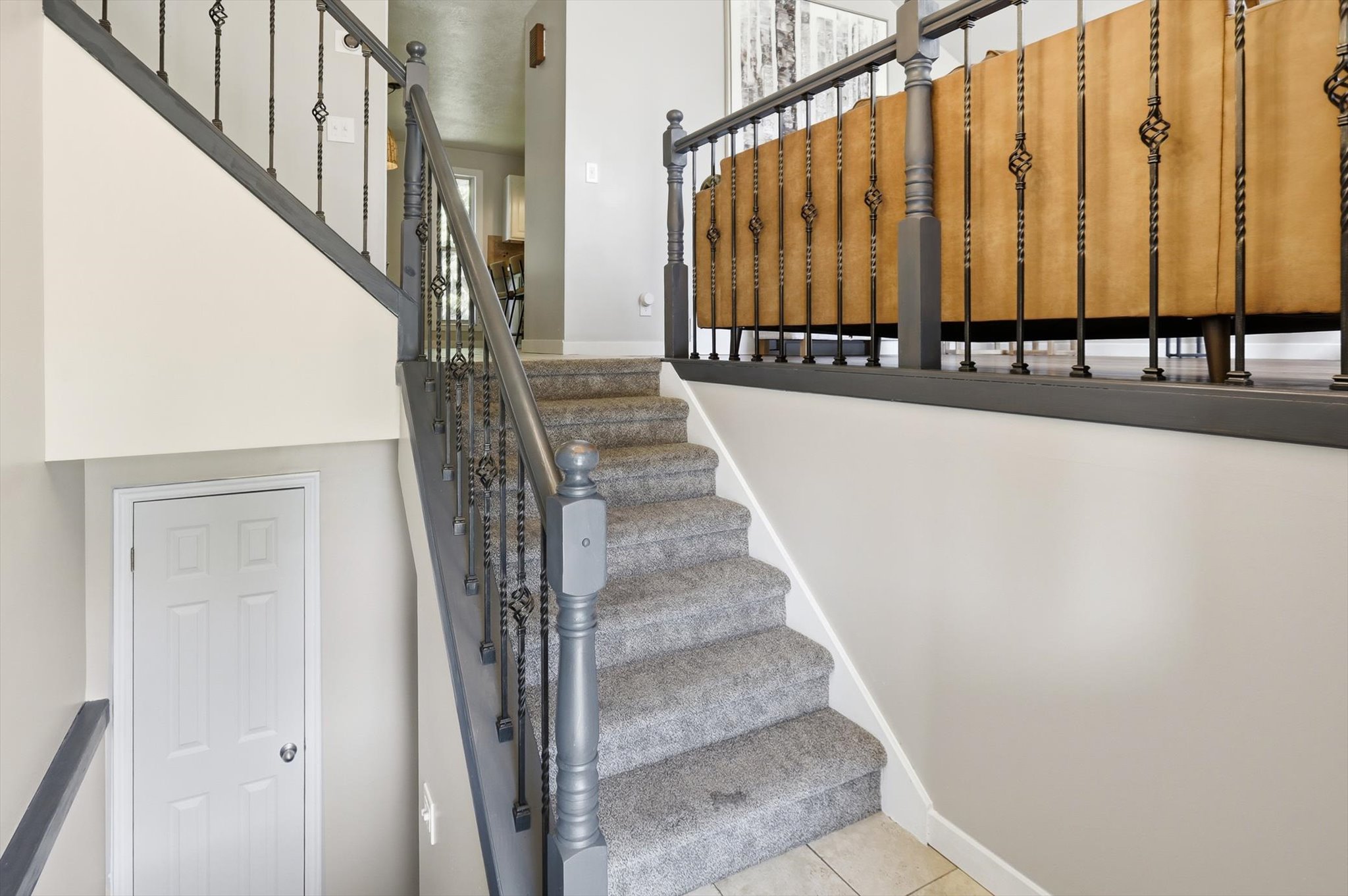 Carpeted staircase featuring painted wood newel posts and handrails, complemented by decorative metal balusters