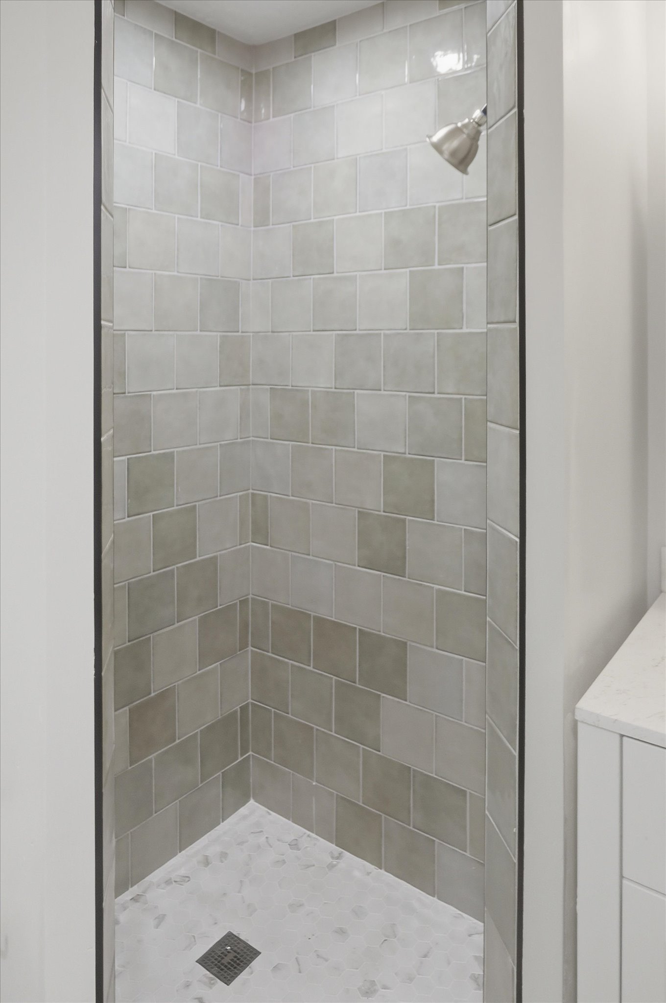 Tiled shower enclosure featuring a satin nickel showerhead, a chevron pattern tile design, and a stone-look shower pan with a square drain