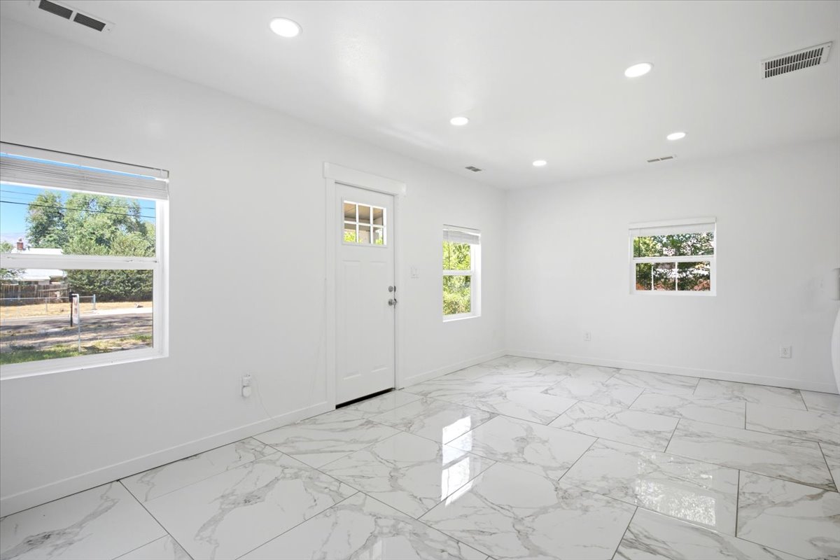 Spacious room featuring large format marble-look tile flooring, white painted walls, recessed ceiling lighting, and multiple windows