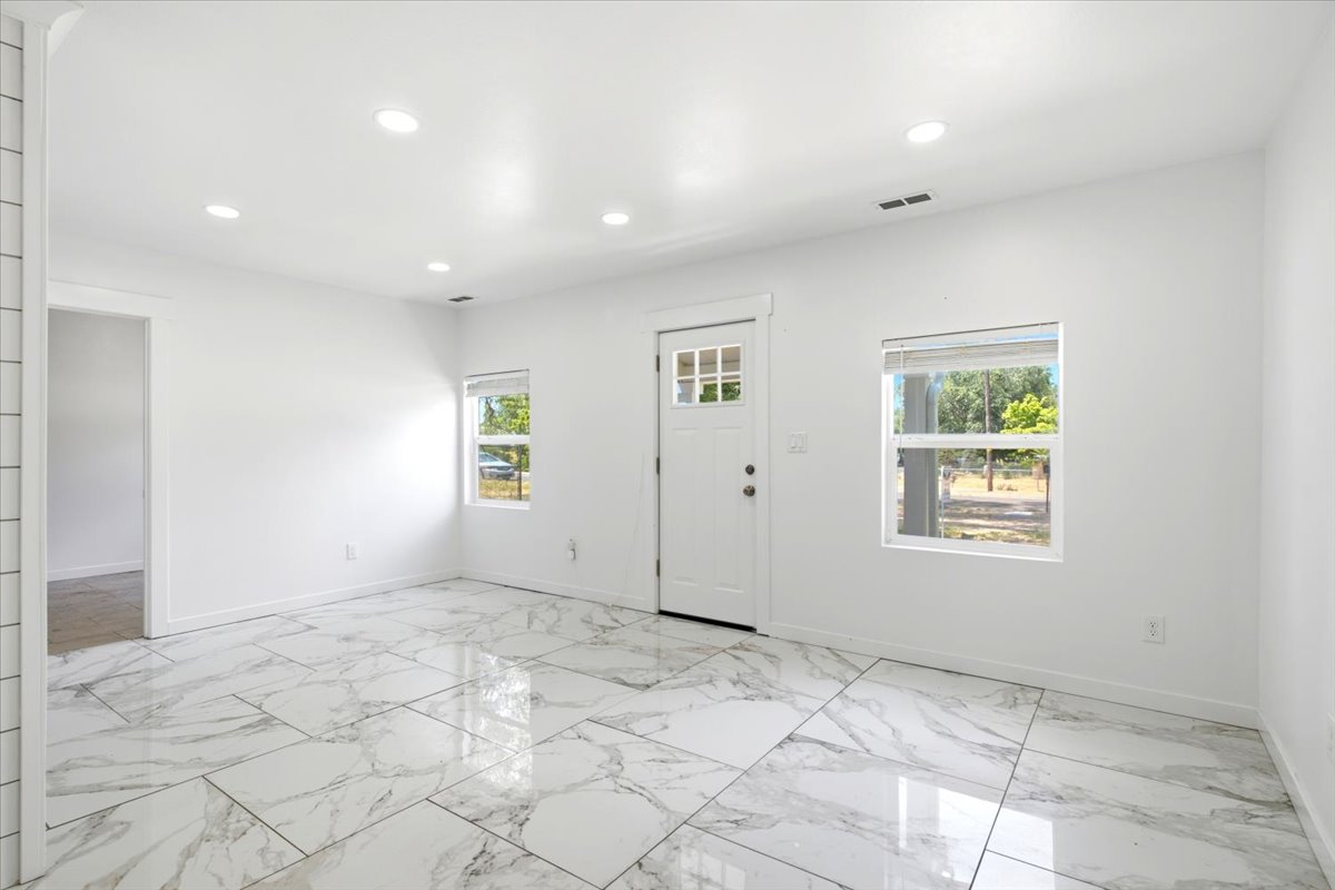 Spacious room featuring large format tile flooring, recessed lighting, white walls, multiple windows, and a panel door with decorative glass inserts