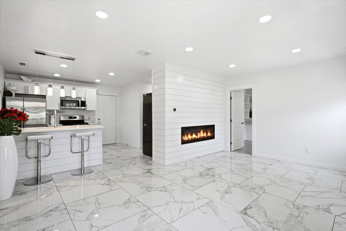 Open-concept living area featuring a linear fireplace, white shiplap accent wall, recessed lighting, and large format marble-look tile flooring
