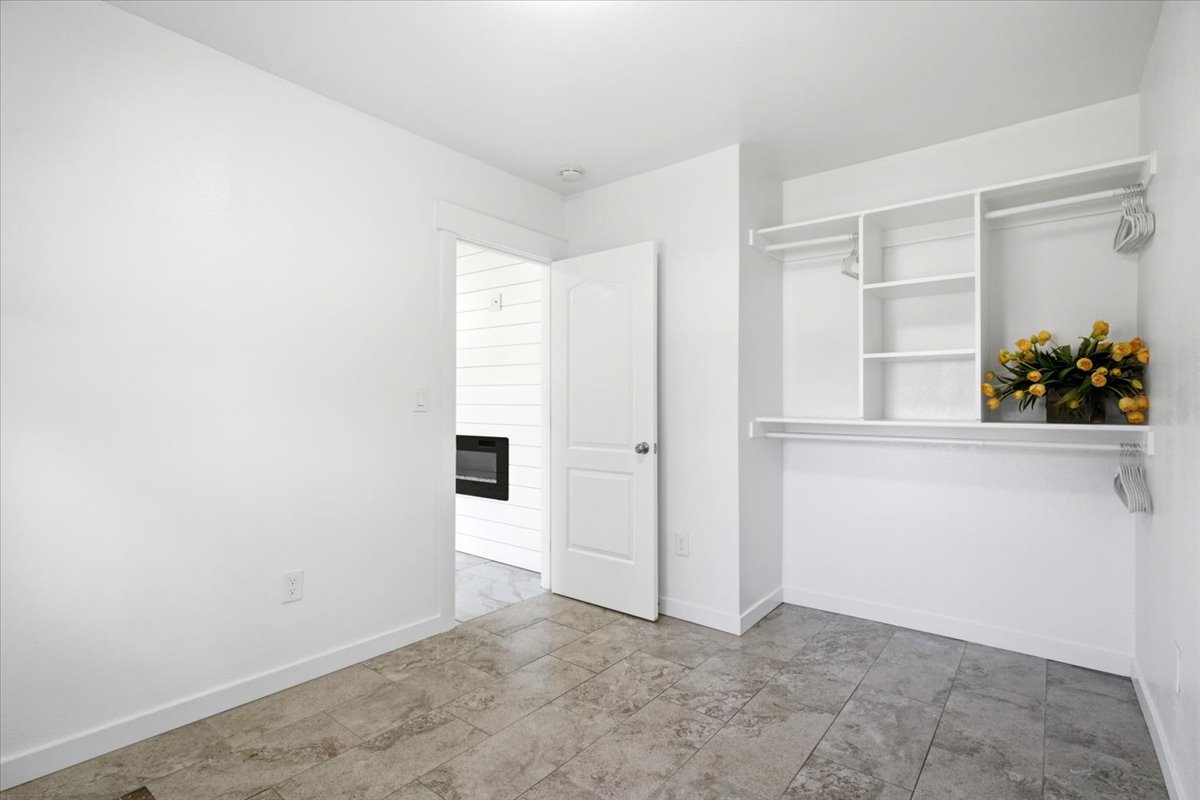 Room featuring neutral-toned tile flooring, white walls, and a built-in closet system