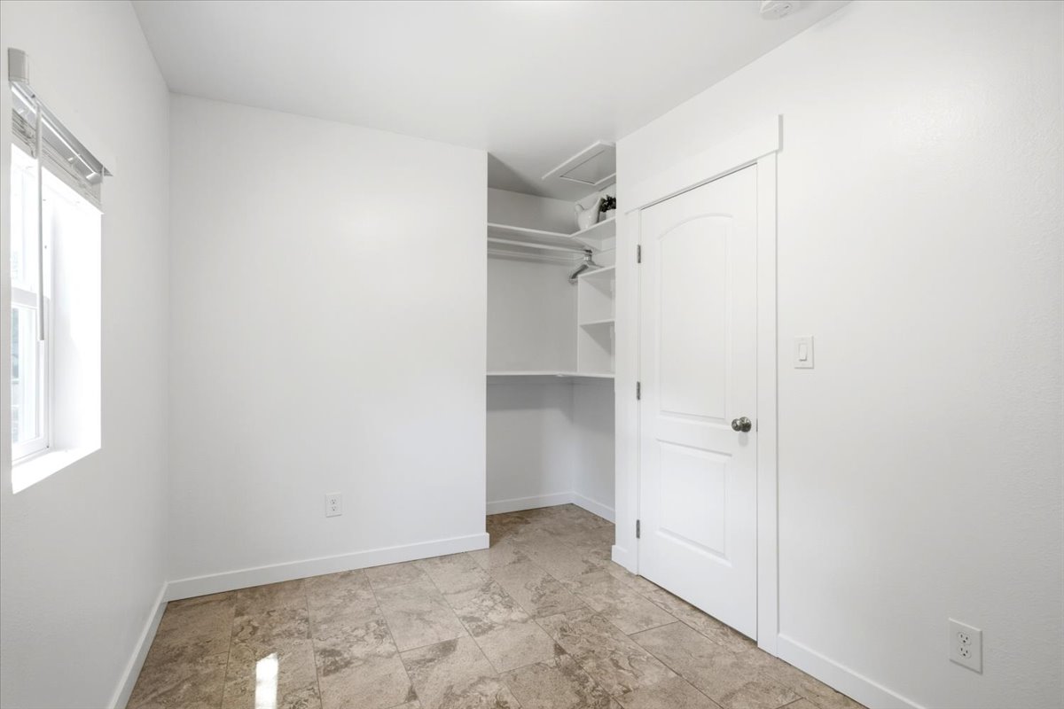 Room featuring neutral wall finishes, tile flooring, a window with horizontal blinds, built-in closet shelving, and a paneled interior door
