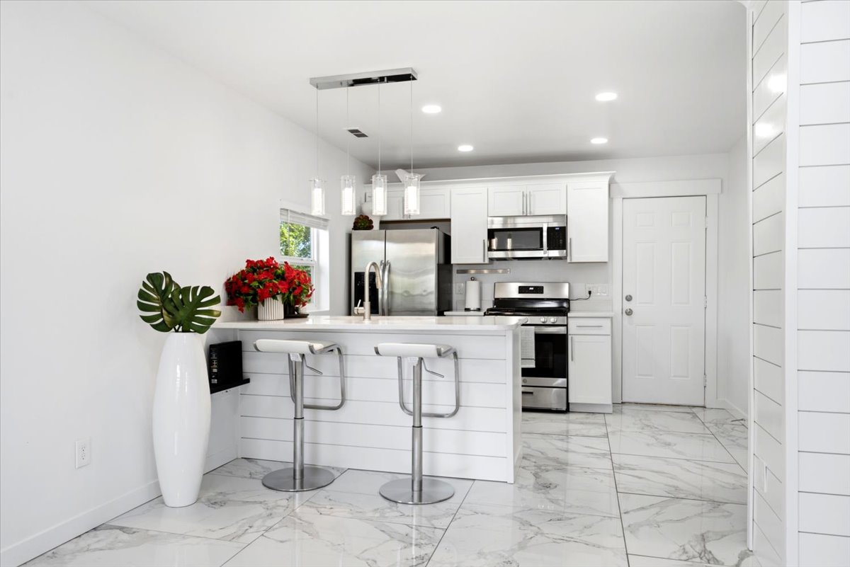 Modern kitchen featuring white cabinetry, stainless steel appliances, a white island with shiplap-style paneling, and marble-look tile flooring