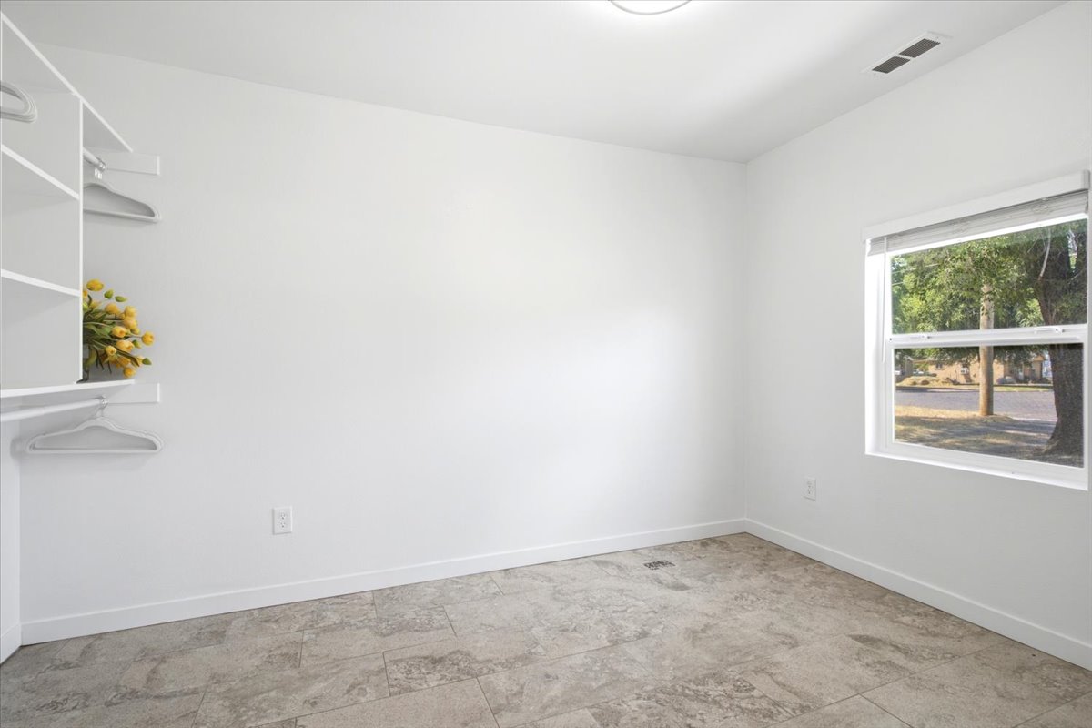 Bright room featuring a window with street views, light gray tile flooring, and a built-in closet system with open shelving and hanging rods