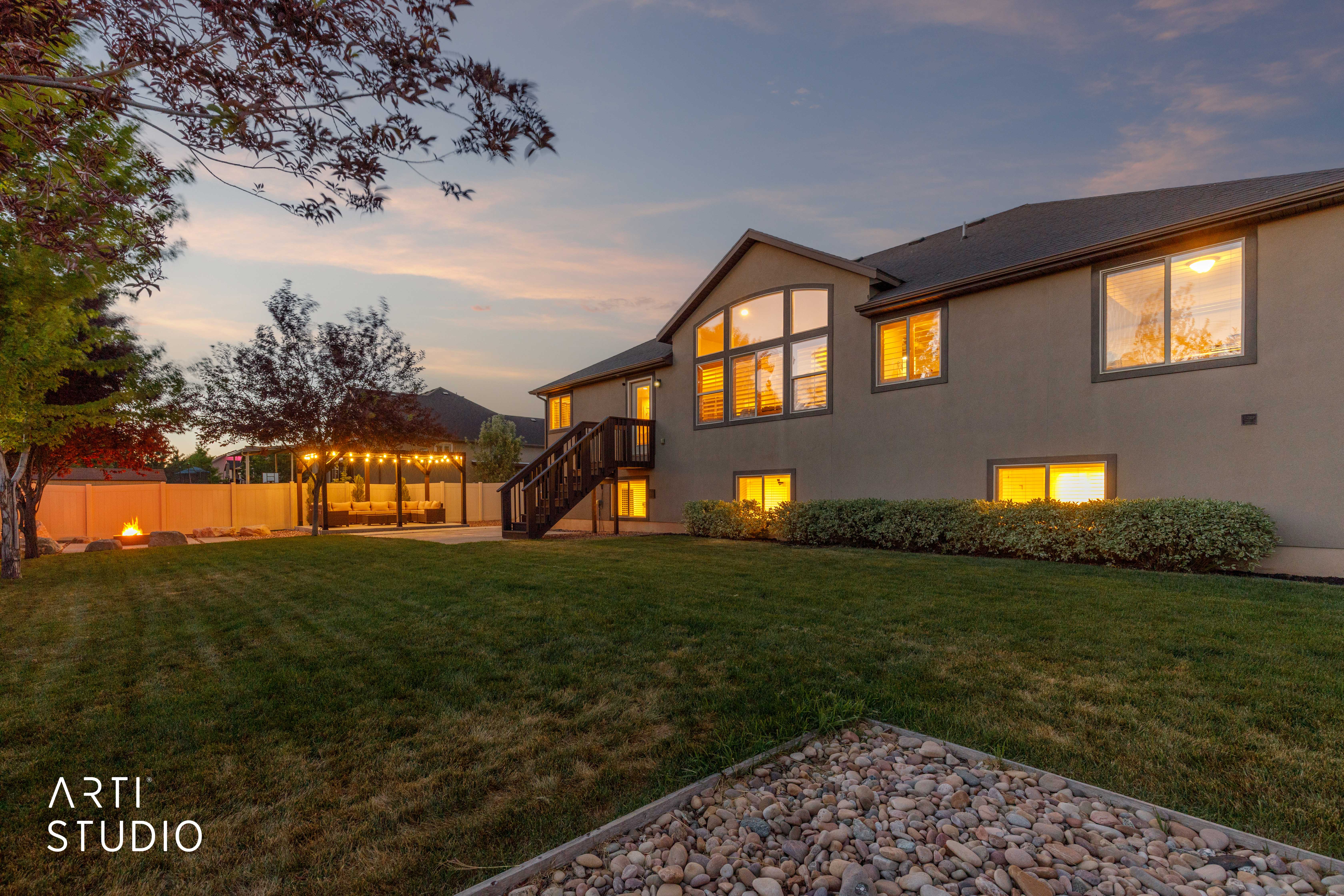 Expansive backyard featuring a manicured lawn, a string-lit pergola, and a visible fire pit area
