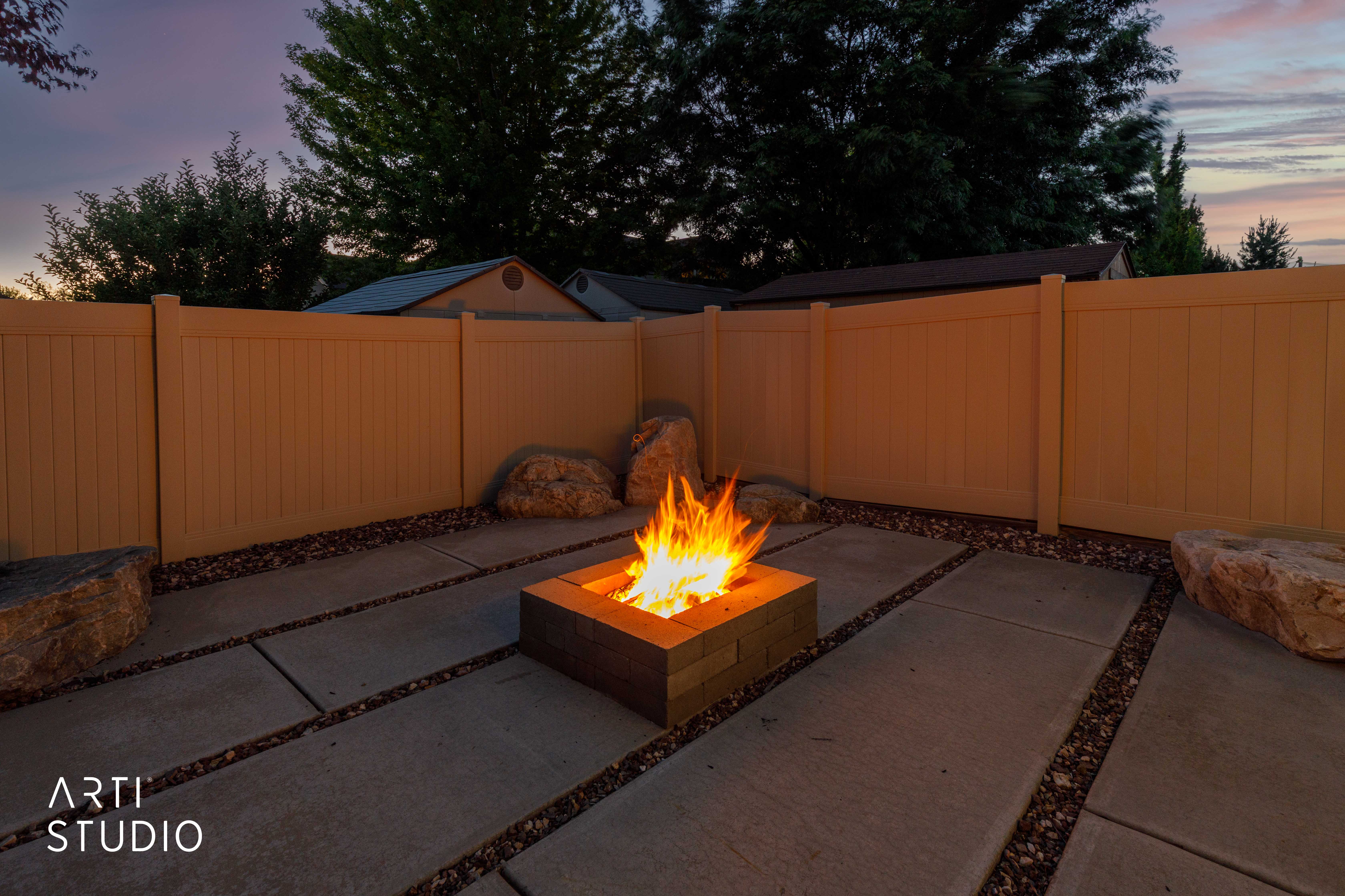 Outdoor patio featuring a built-in fire pit, concrete paver sections, and dark aggregate ground cover