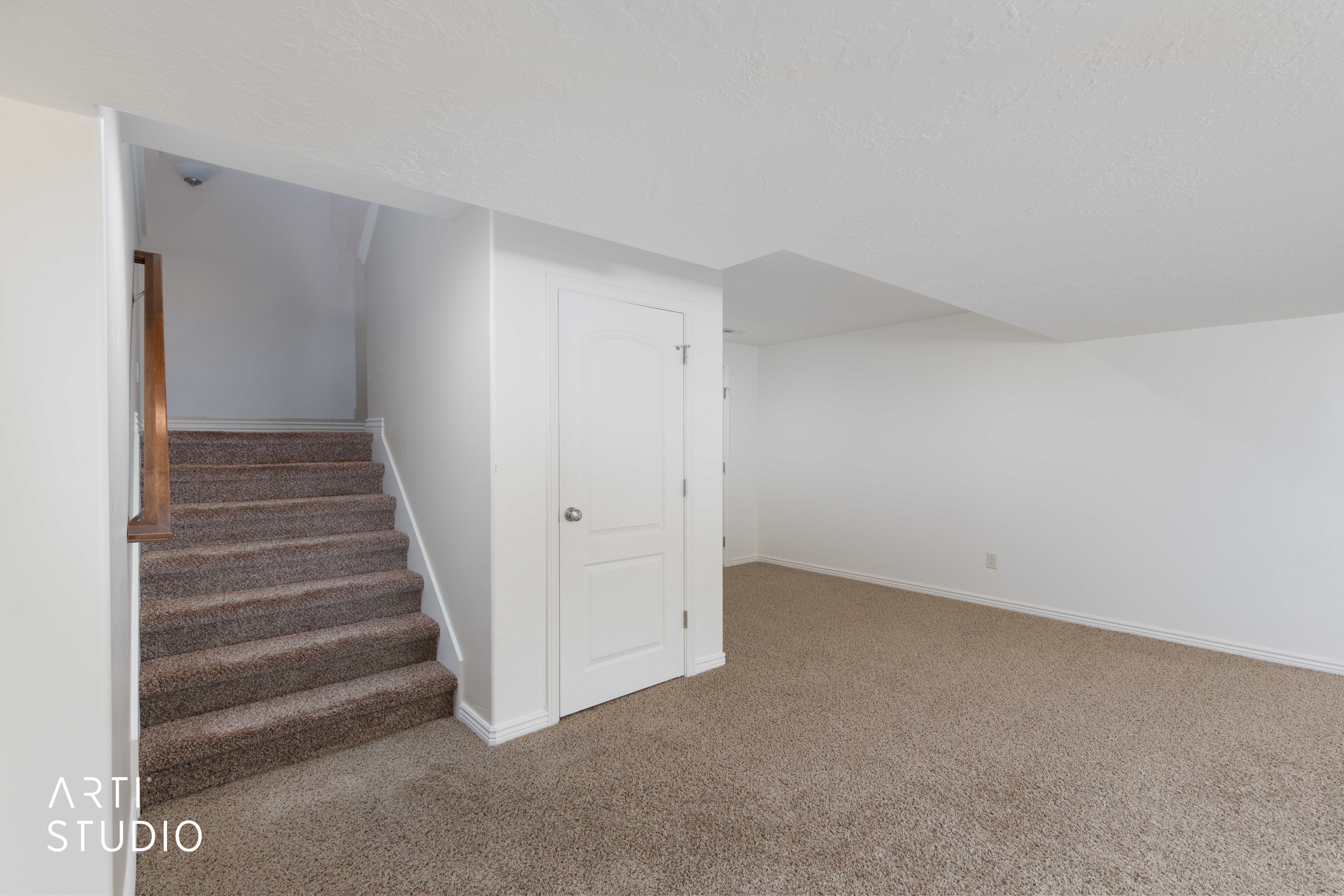 Carpeted staircase with wood handrail, white walls, and neutral carpet flooring