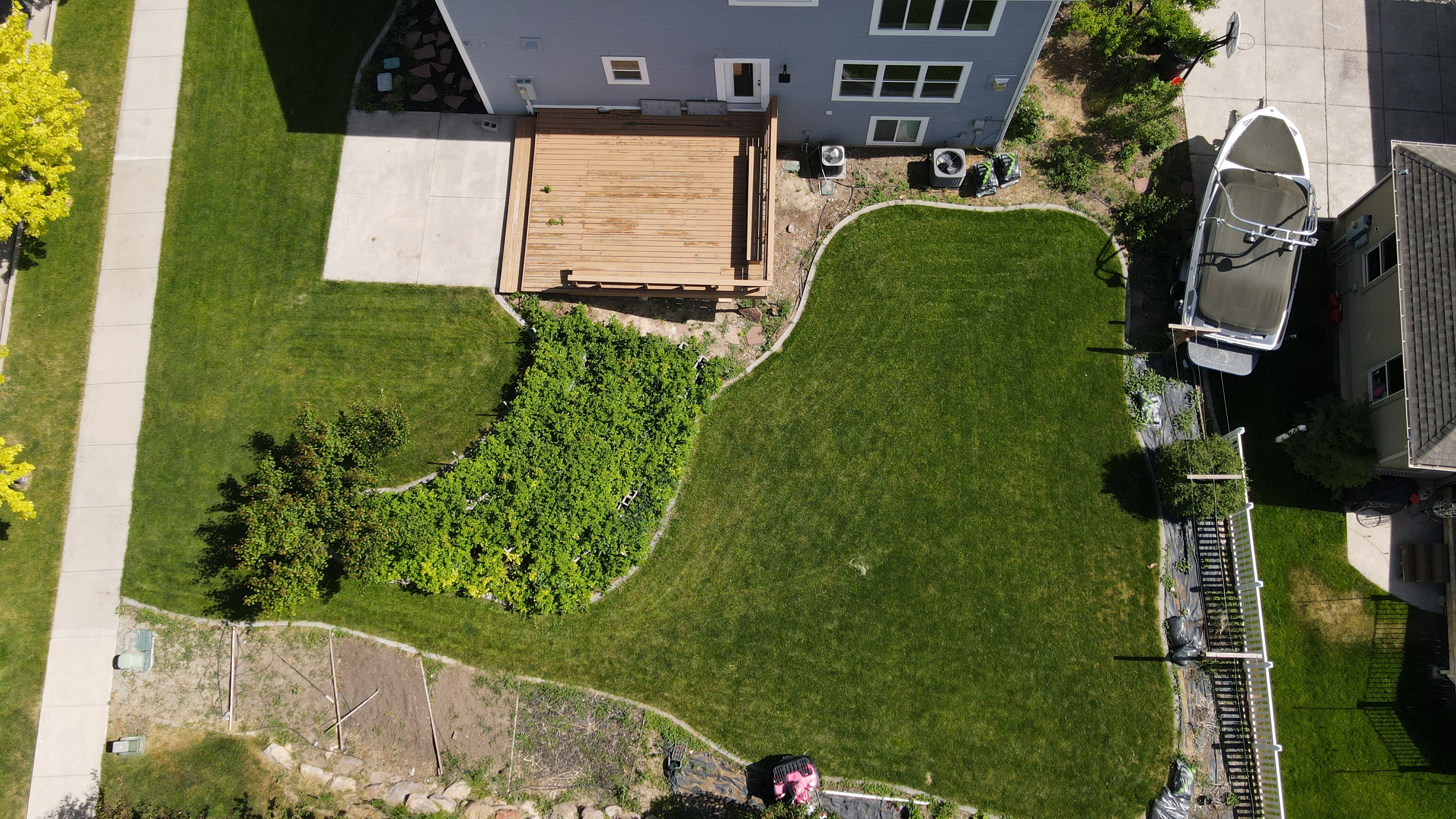 Expansive backyard featuring a manicured lawn, a wood deck, a concrete patio, and garden beds