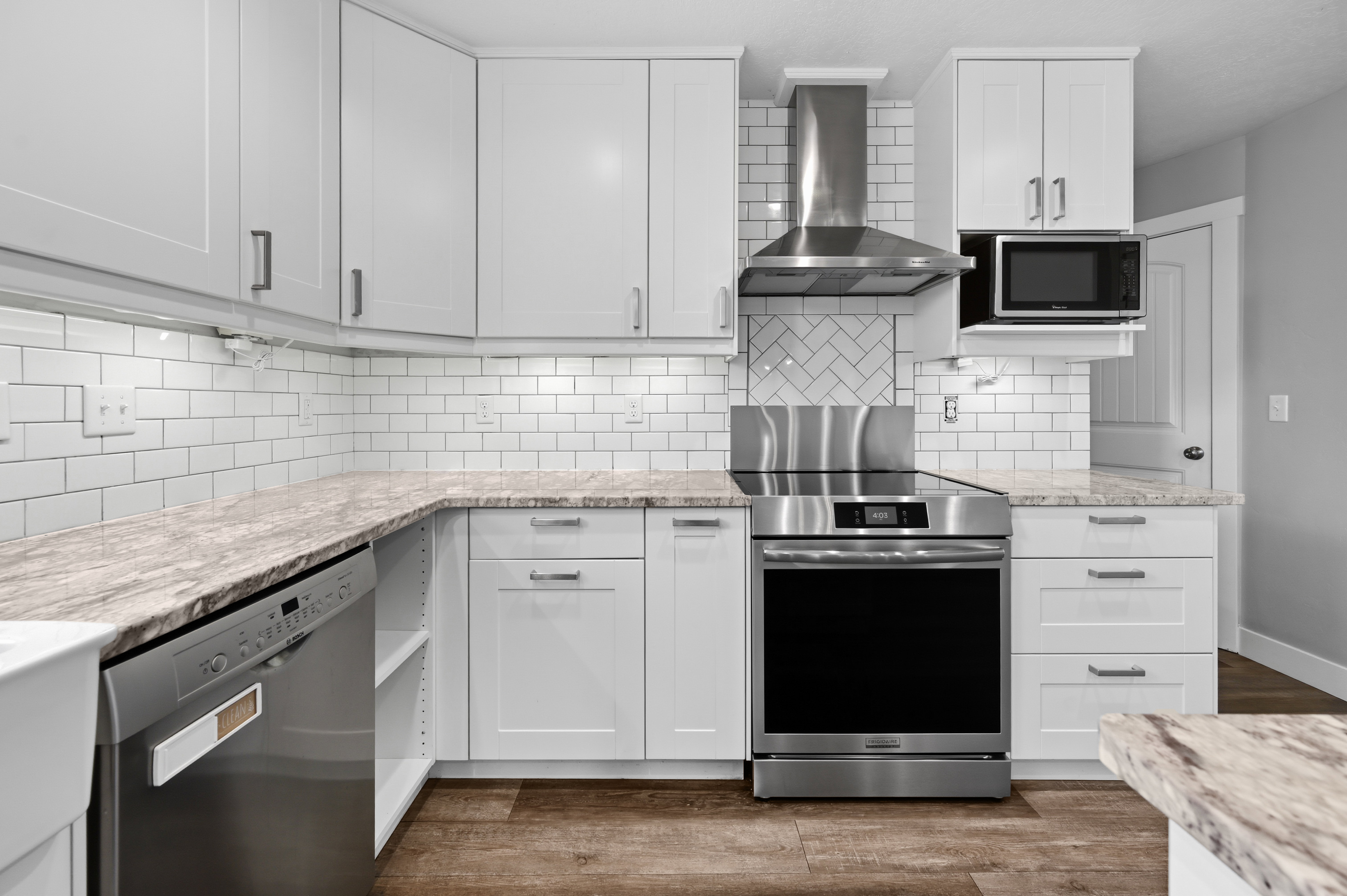 Modern kitchen featuring white shaker cabinetry, stainless steel appliances, a subway tile backsplash, light-colored countertops, and wood-finish flooring