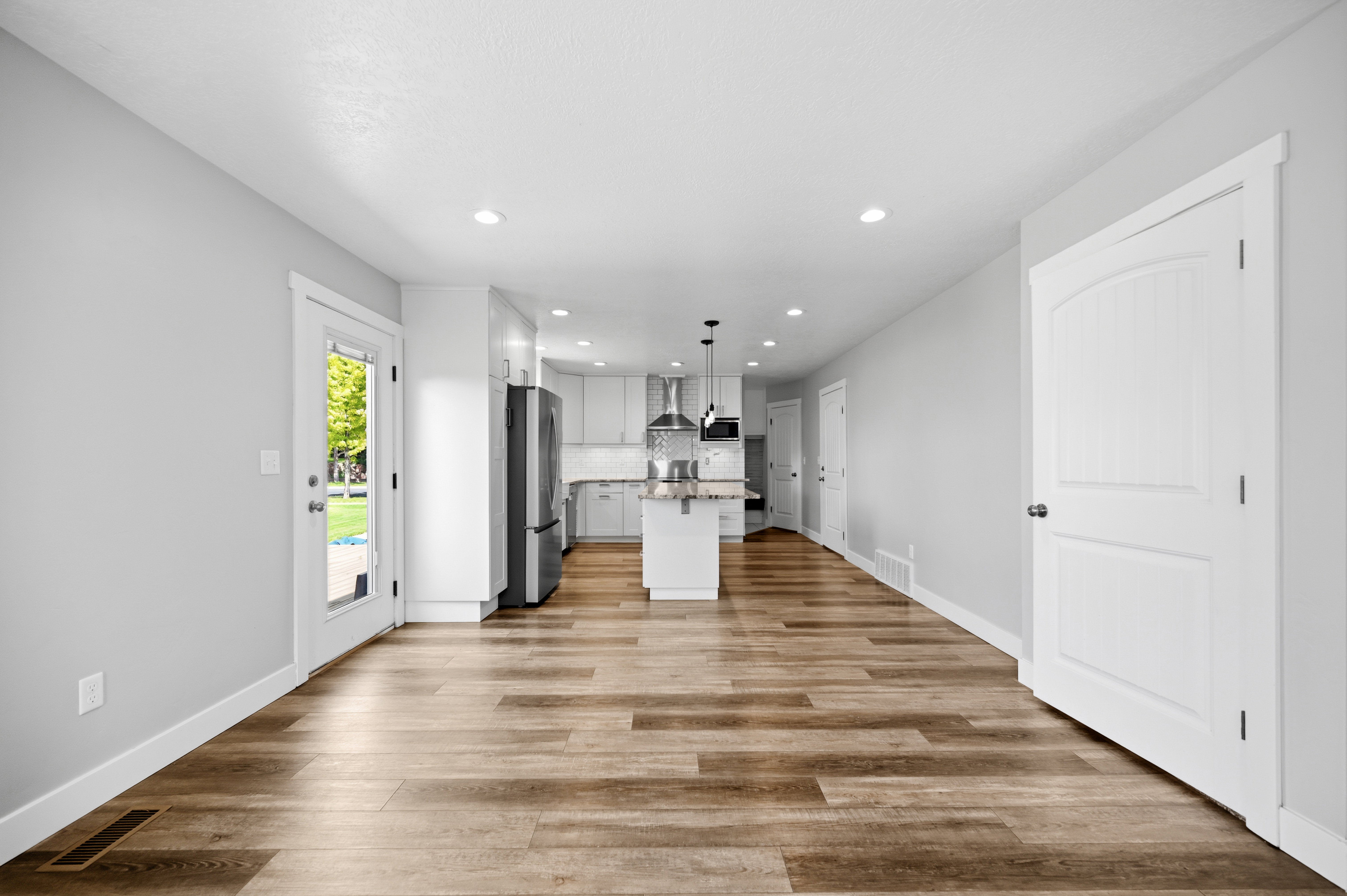 Open-concept main living area featuring wood-finish flooring, recessed lighting, and a kitchen with white cabinetry and stainless steel appliances