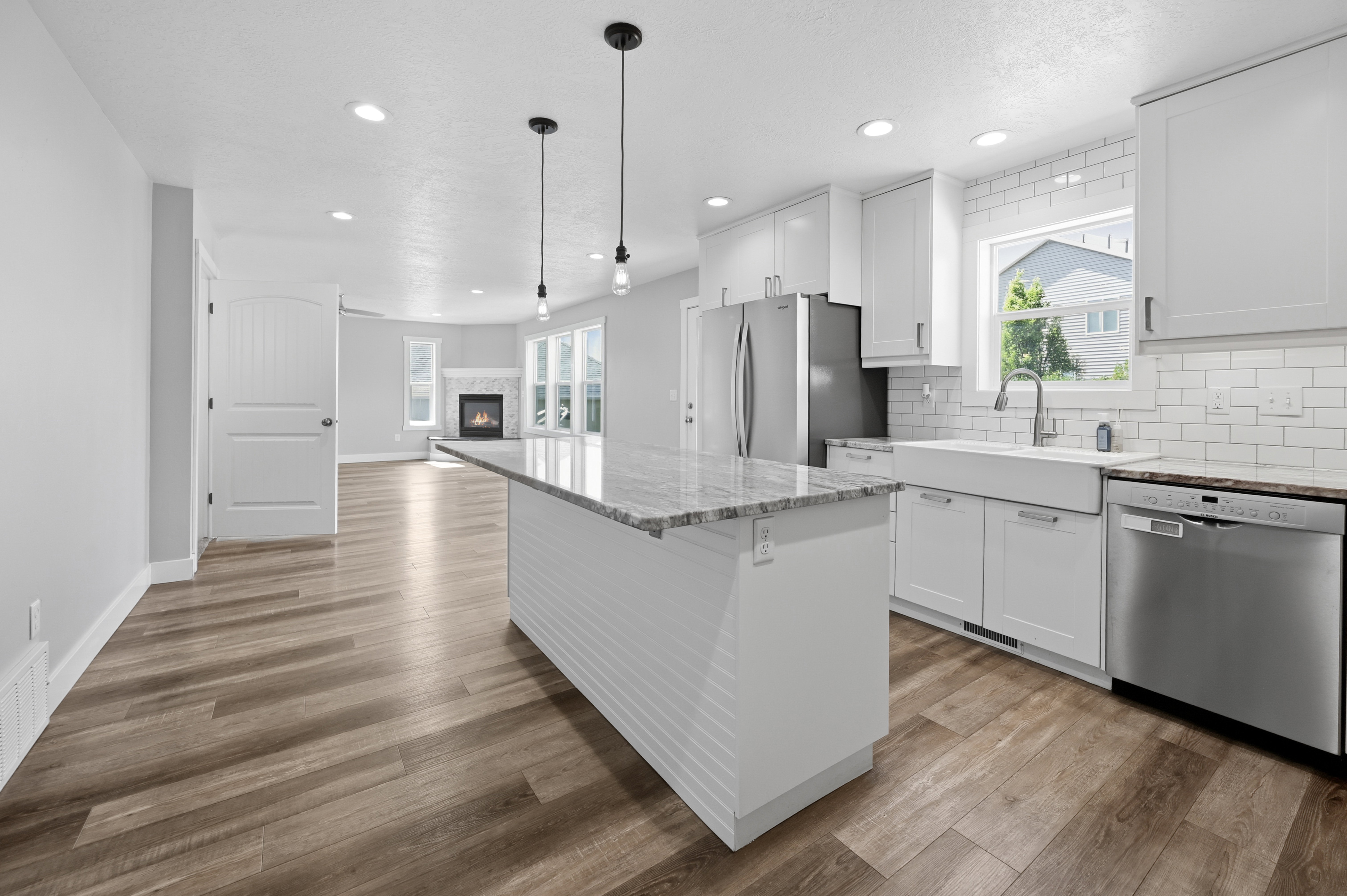 Modern kitchen featuring a large center island with a granite-style countertop, white shaker cabinetry, stainless steel appliances, and a farmhouse sink