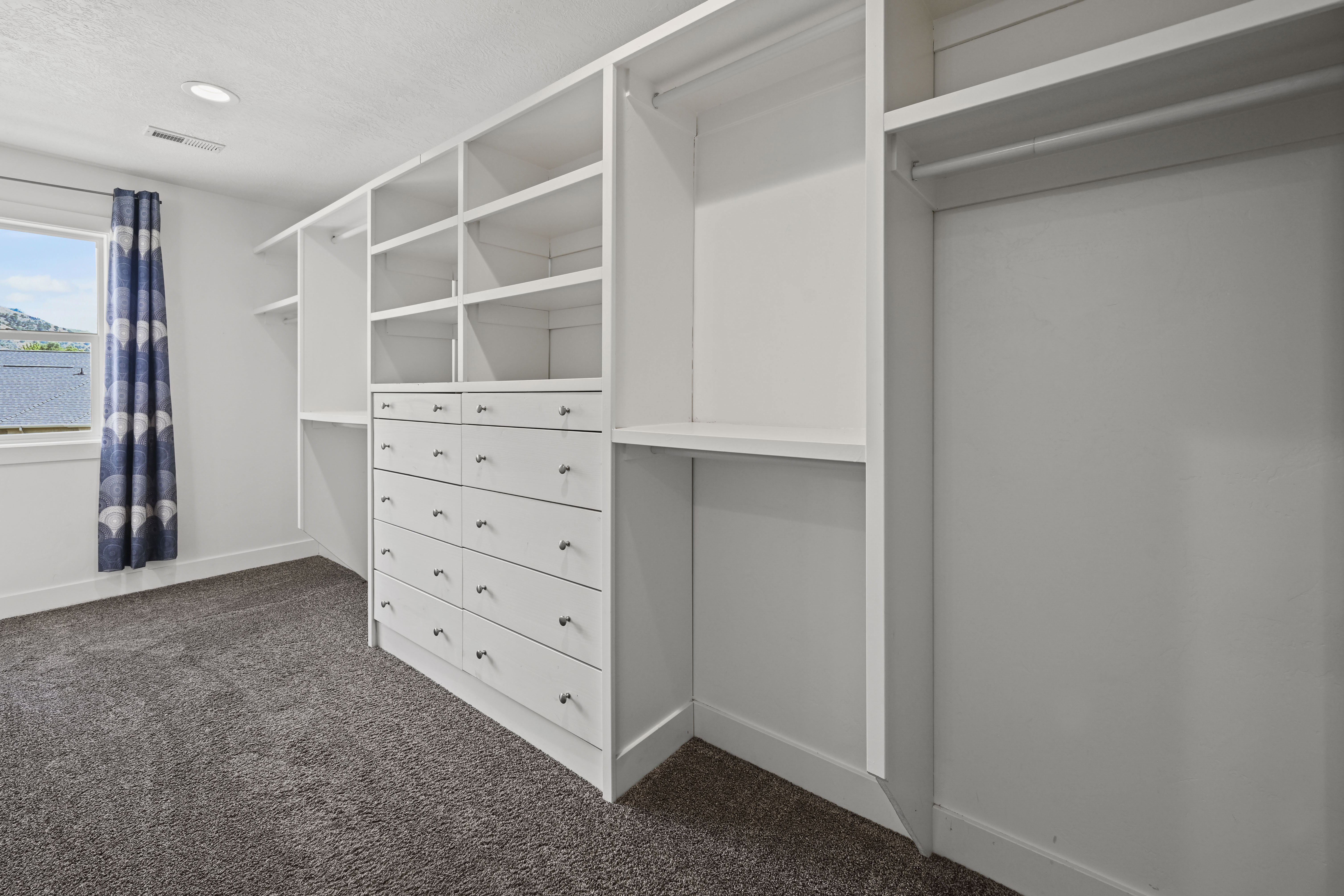 Custom built-in white cabinetry featuring multiple drawers with black hardware, open shelving, and hanging rods