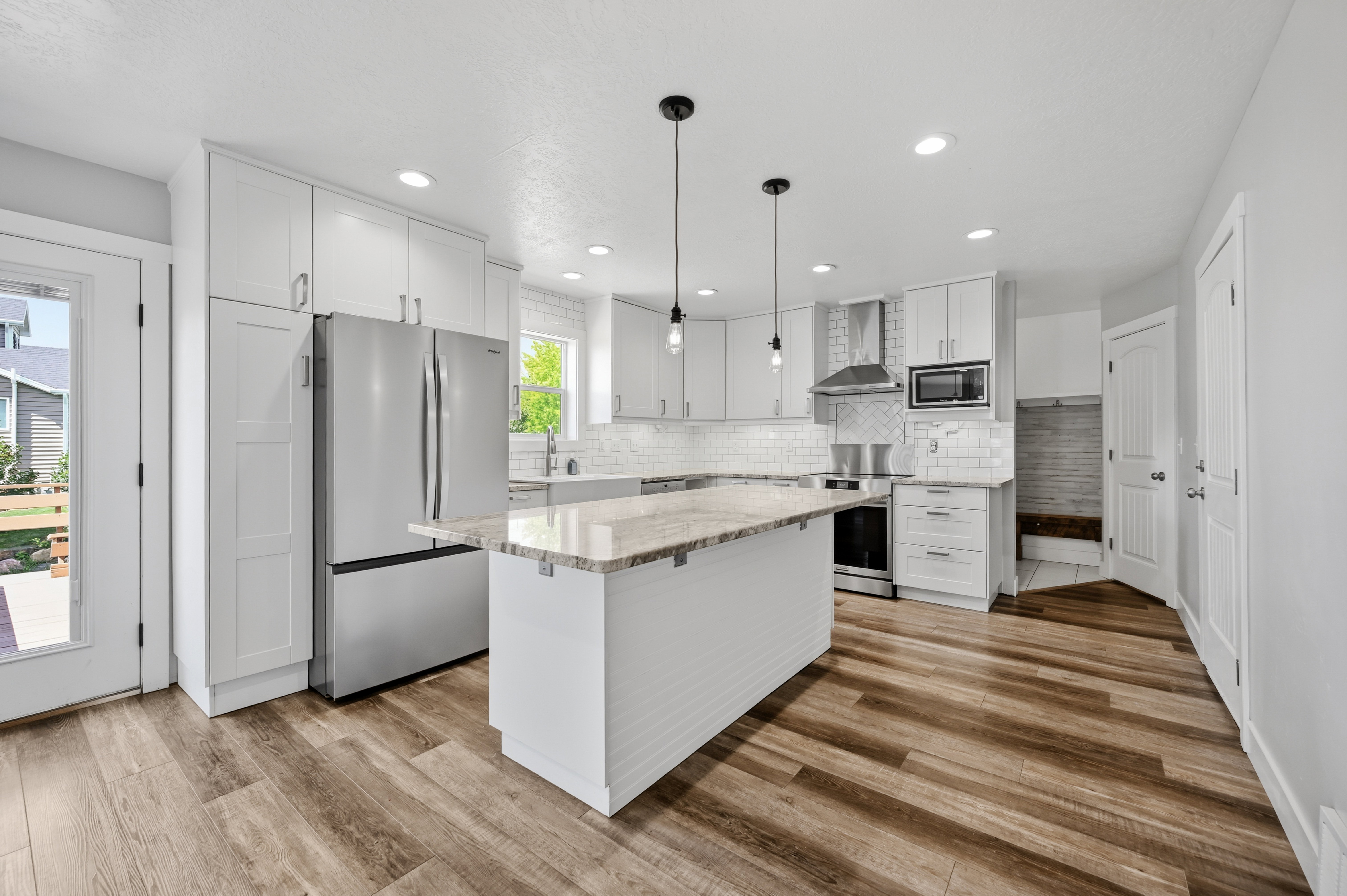 Modern kitchen featuring white cabinetry, stainless steel appliances, a center island with a light-toned countertop, wood-finish flooring, and a subway tile backsplash