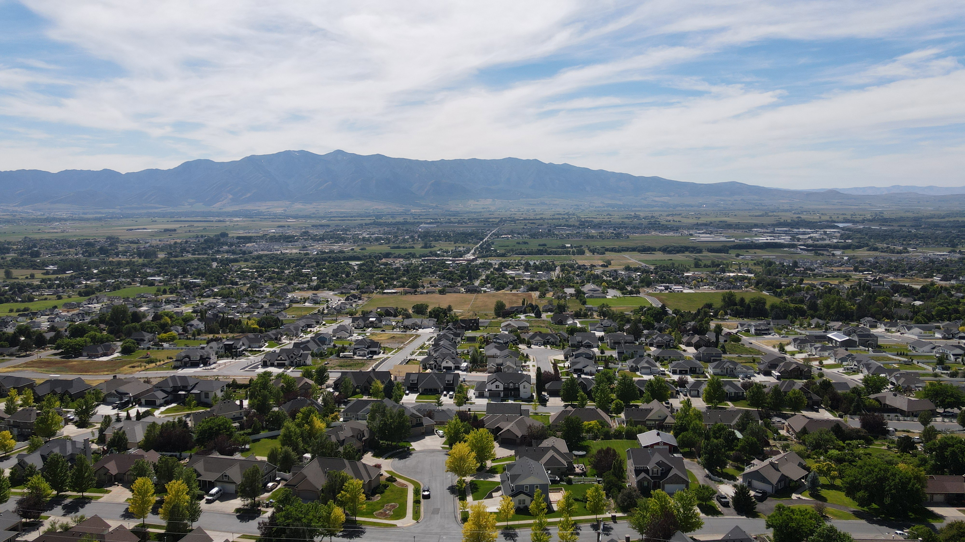 Expansive residential area featuring numerous single-family homes, mature trees, and paved streets, with a distant mountain range backdrop