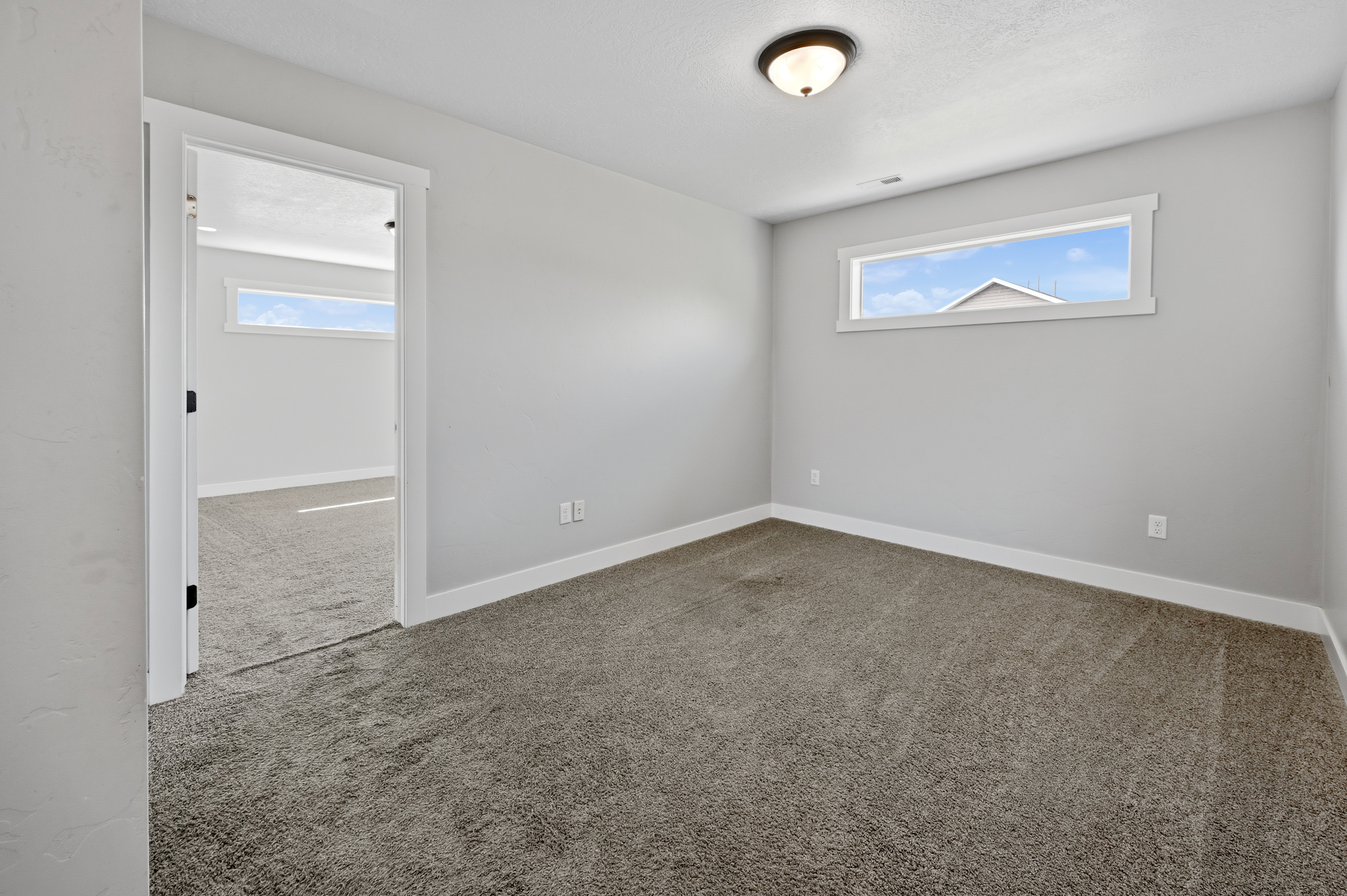 Carpeted room with a horizontal transom window, white trim, light gray walls, and a semi-flush mount ceiling light fixture