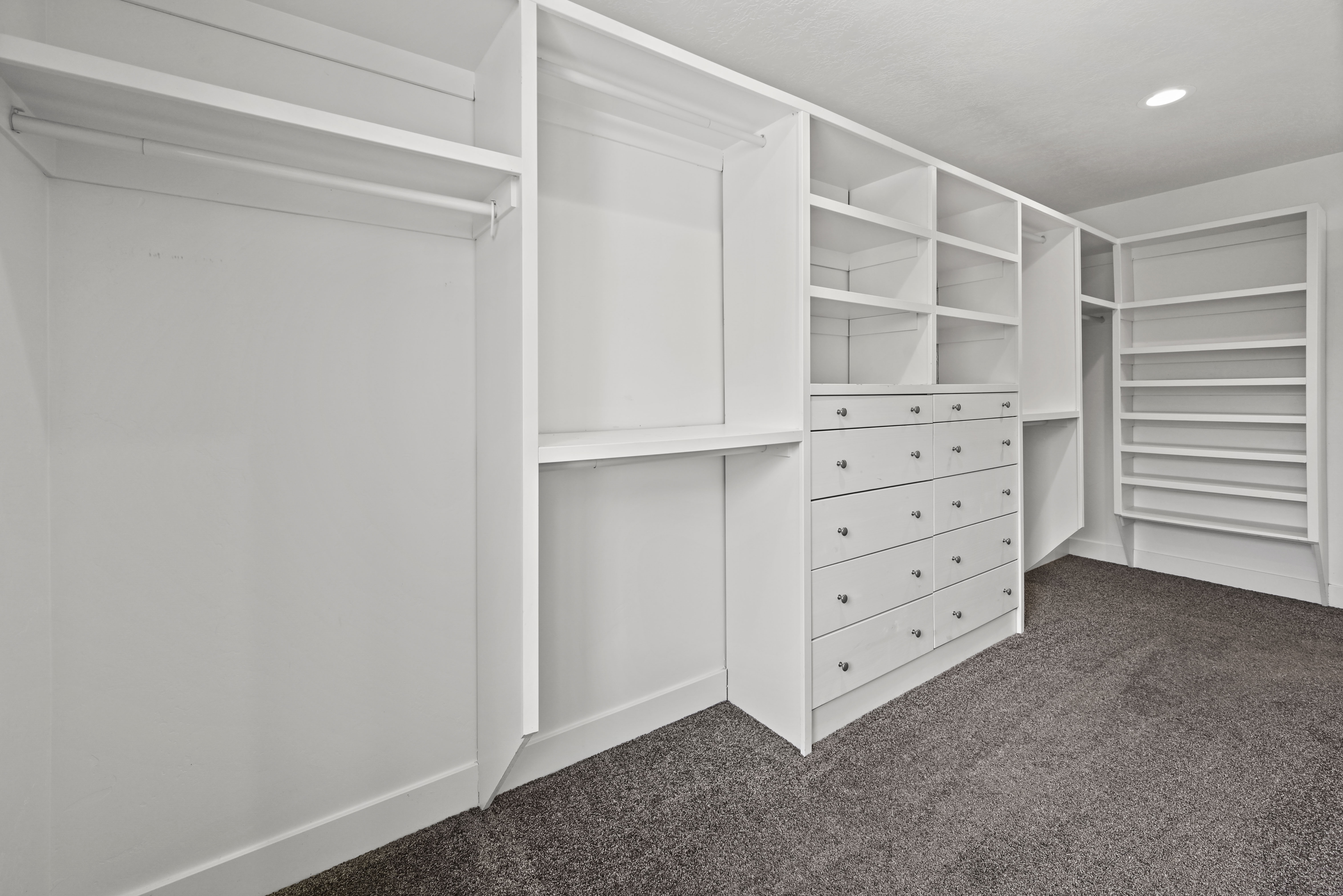 Custom closet system featuring white built-in shelving, hanging rods, and integrated drawer units with silver hardware