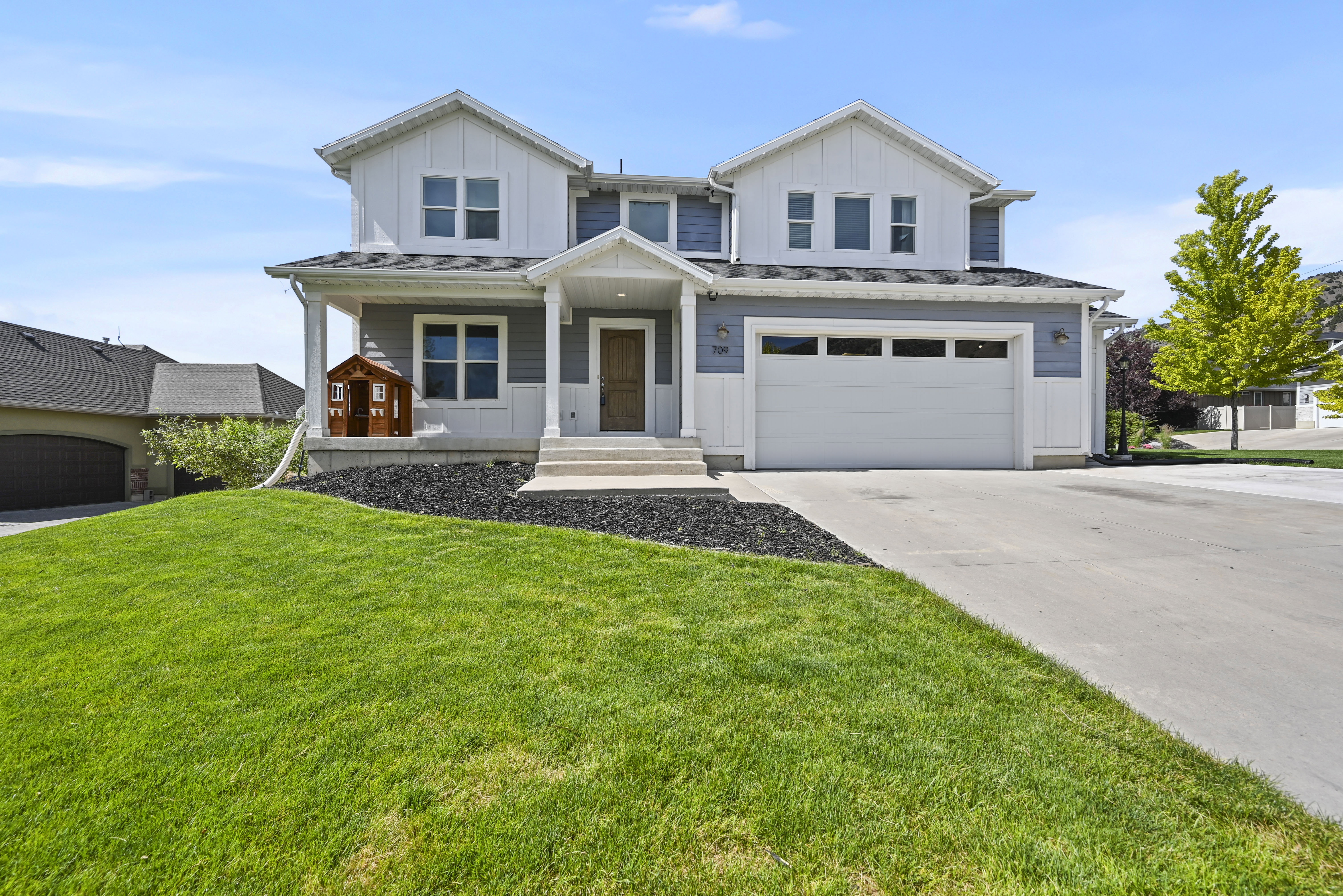 Contemporary two-story residence featuring a two-car garage, white vertical siding, blue horizontal siding, a covered porch, and a concrete driveway