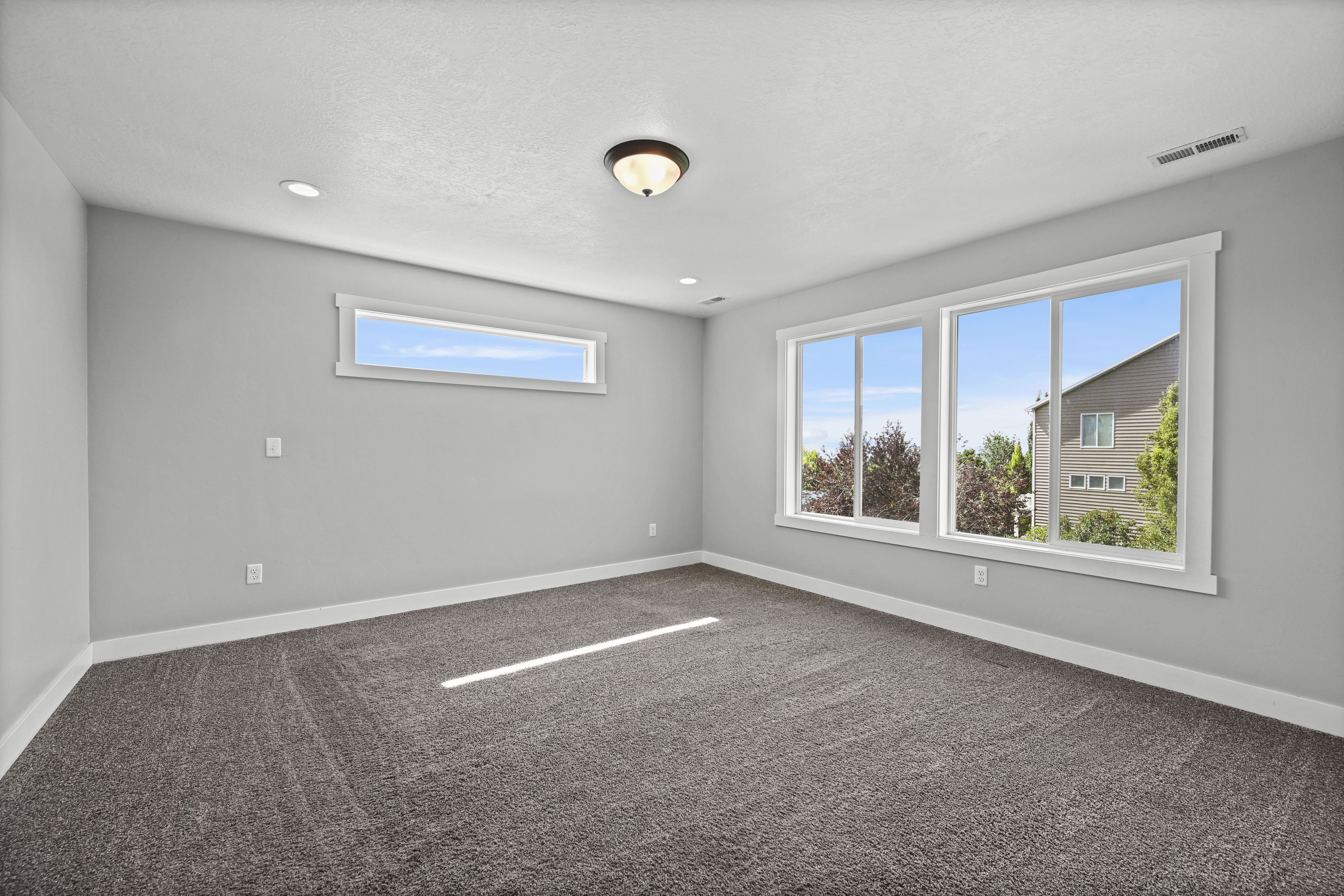 Spacious room featuring neutral carpeting, light gray walls, a large three-panel window, a high horizontal window, and recessed lighting