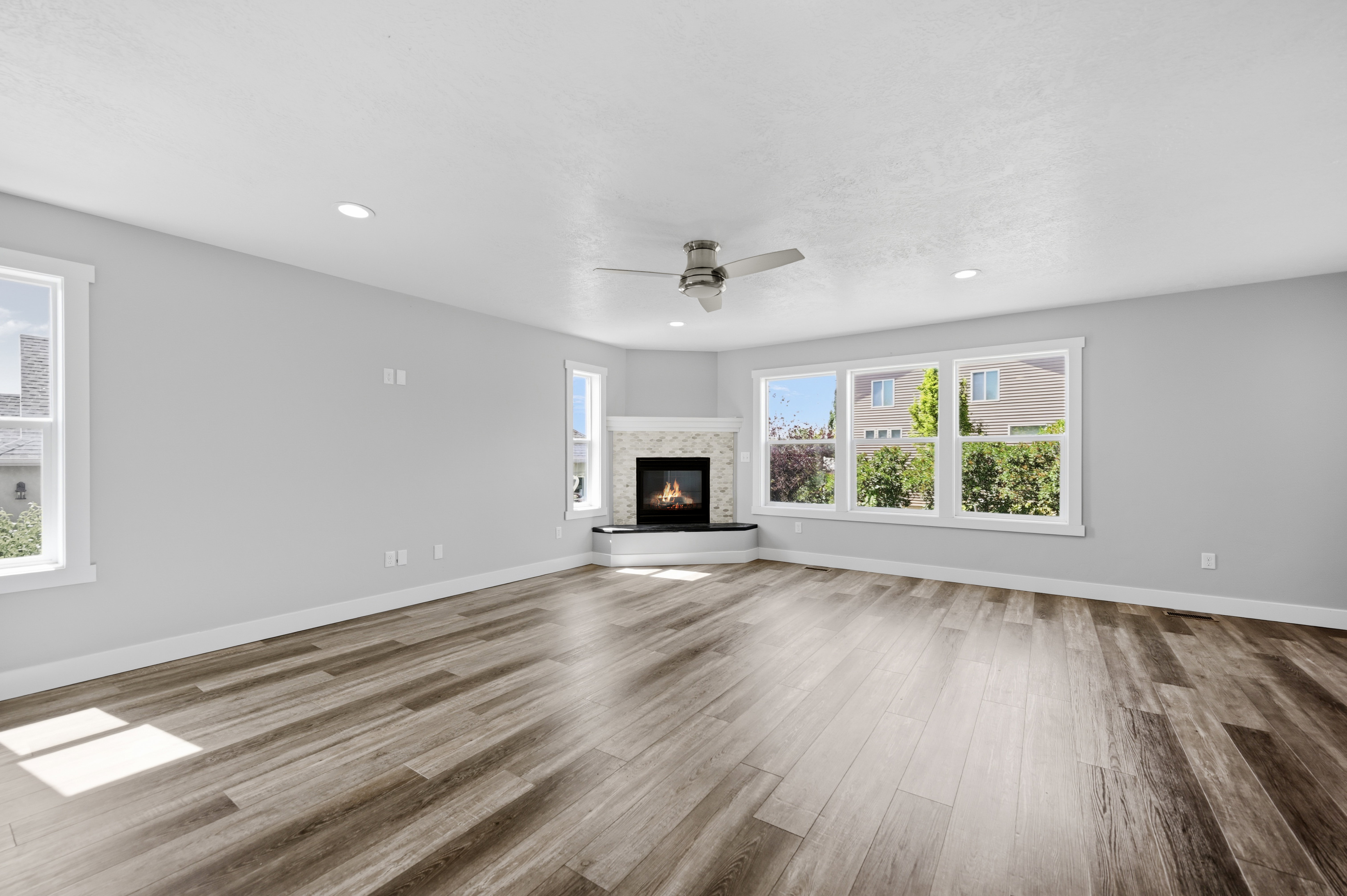 Spacious living area featuring wood-finish flooring, a corner fireplace with a tiled surround, recessed lighting, and a ceiling fan