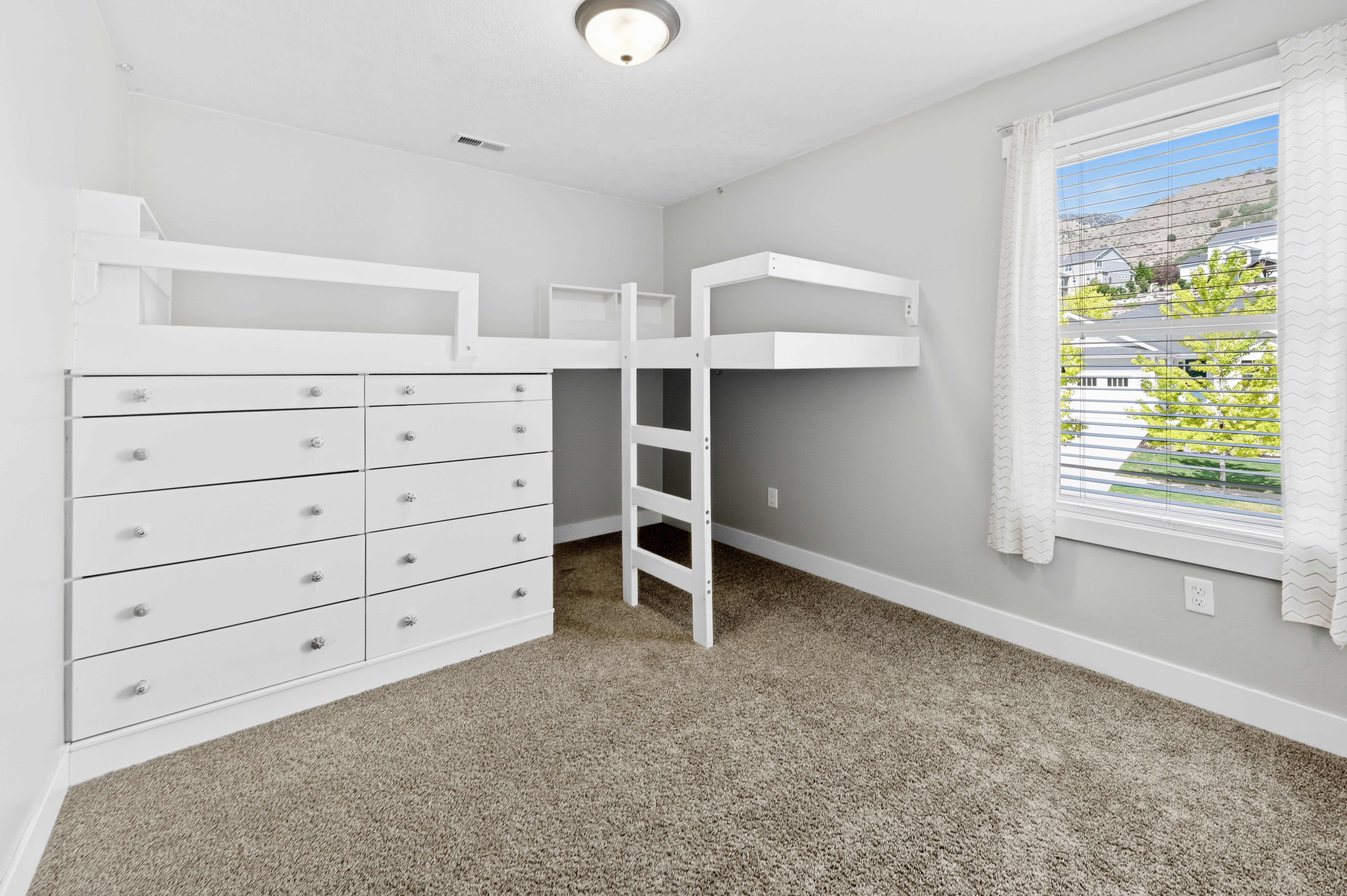 Room featuring a built-in loft bed with integrated dresser storage, a ladder for access, carpet flooring, and a large window with white blinds