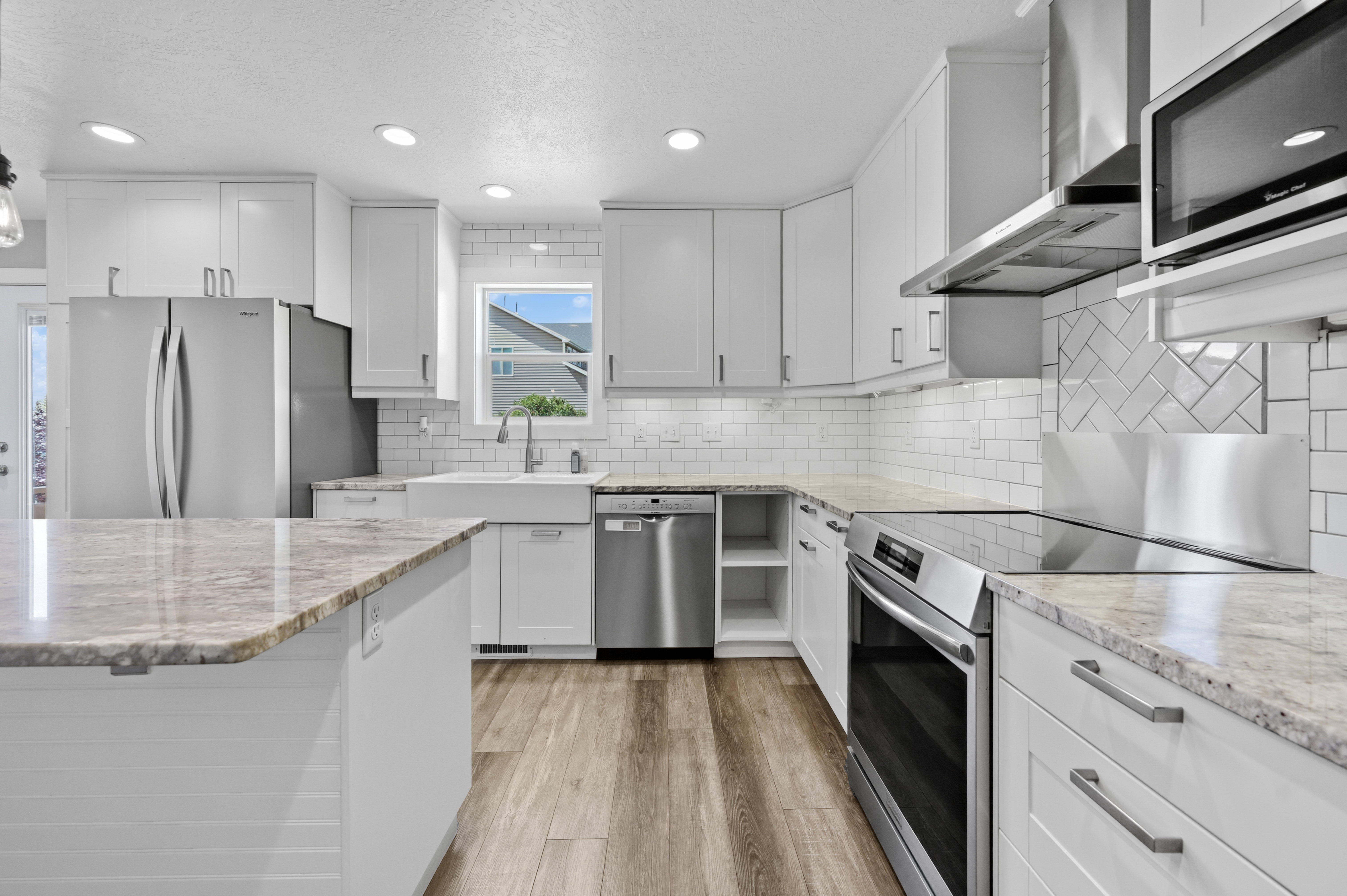 Contemporary kitchen featuring white cabinetry, stainless steel appliances, granite countertops, wood-finish flooring, and a subway tile backsplash