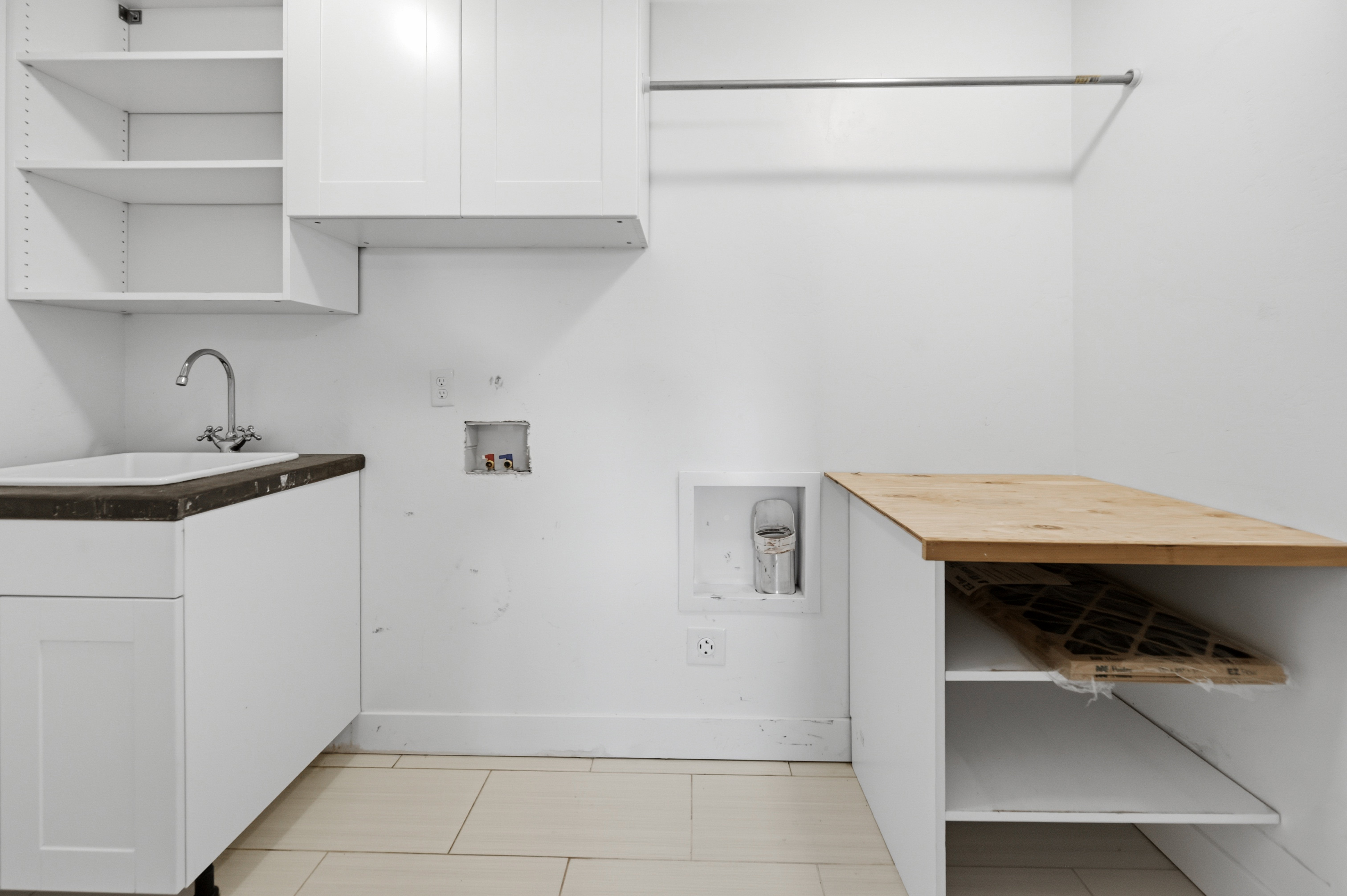 Dedicated laundry space featuring white cabinetry, a utility sink with a chrome faucet, and a built-in wood-finish countertop