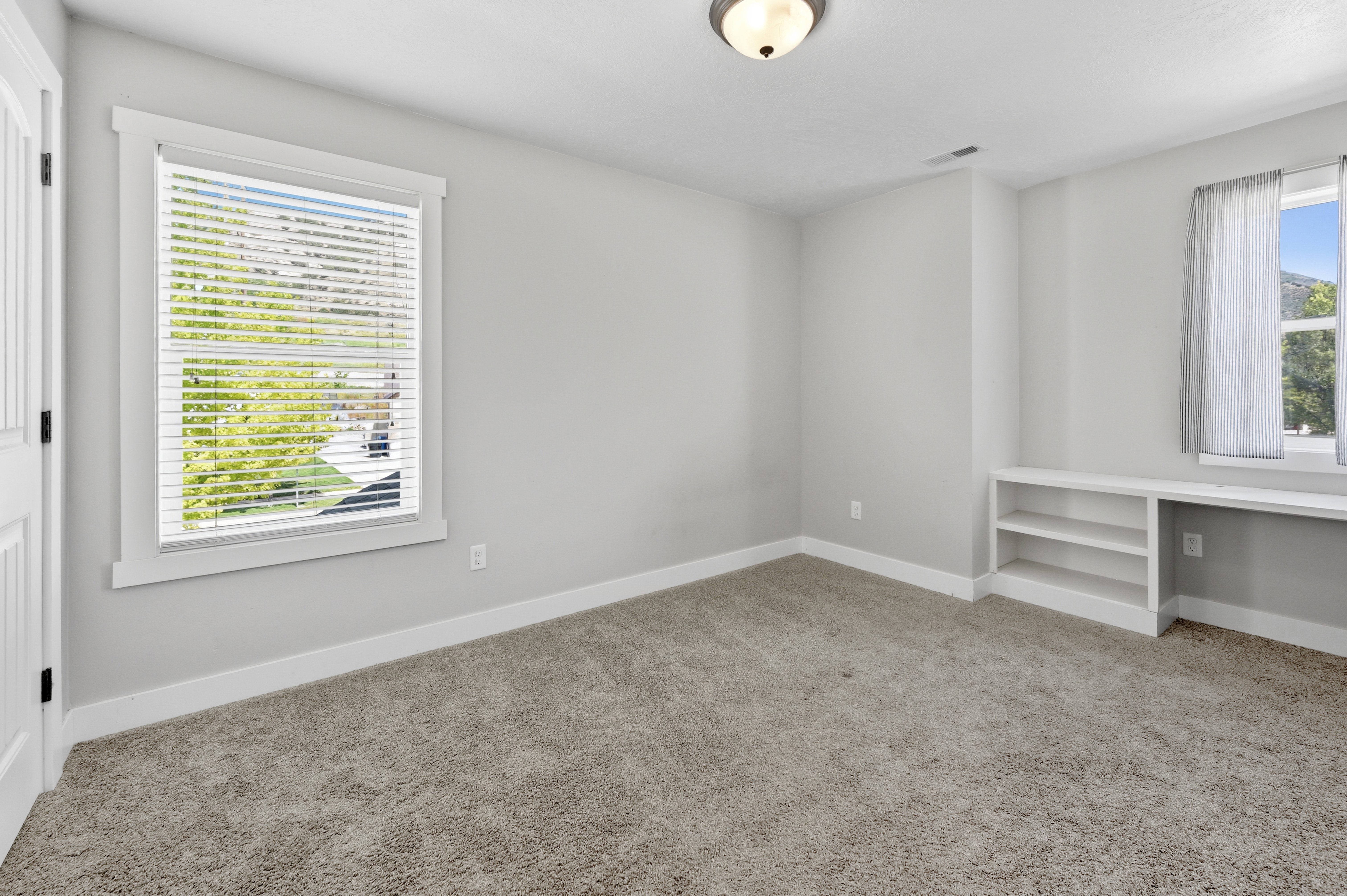 Carpeted room featuring a built-in shelving unit, a window with blinds, and white trim