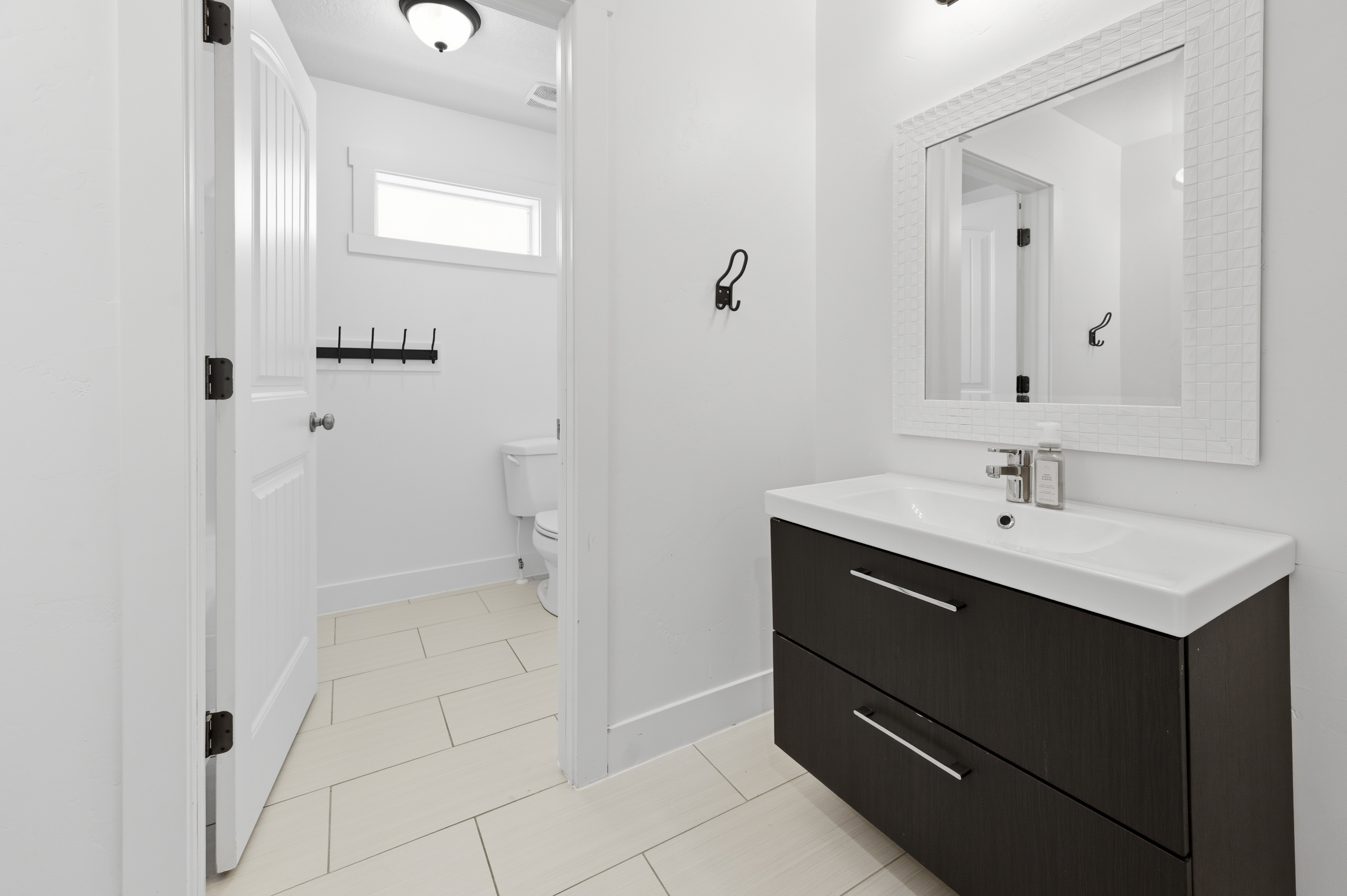 Bathroom featuring a floating dark wood-finish vanity with an integrated white sink, a decorative framed mirror, and light-toned tile flooring