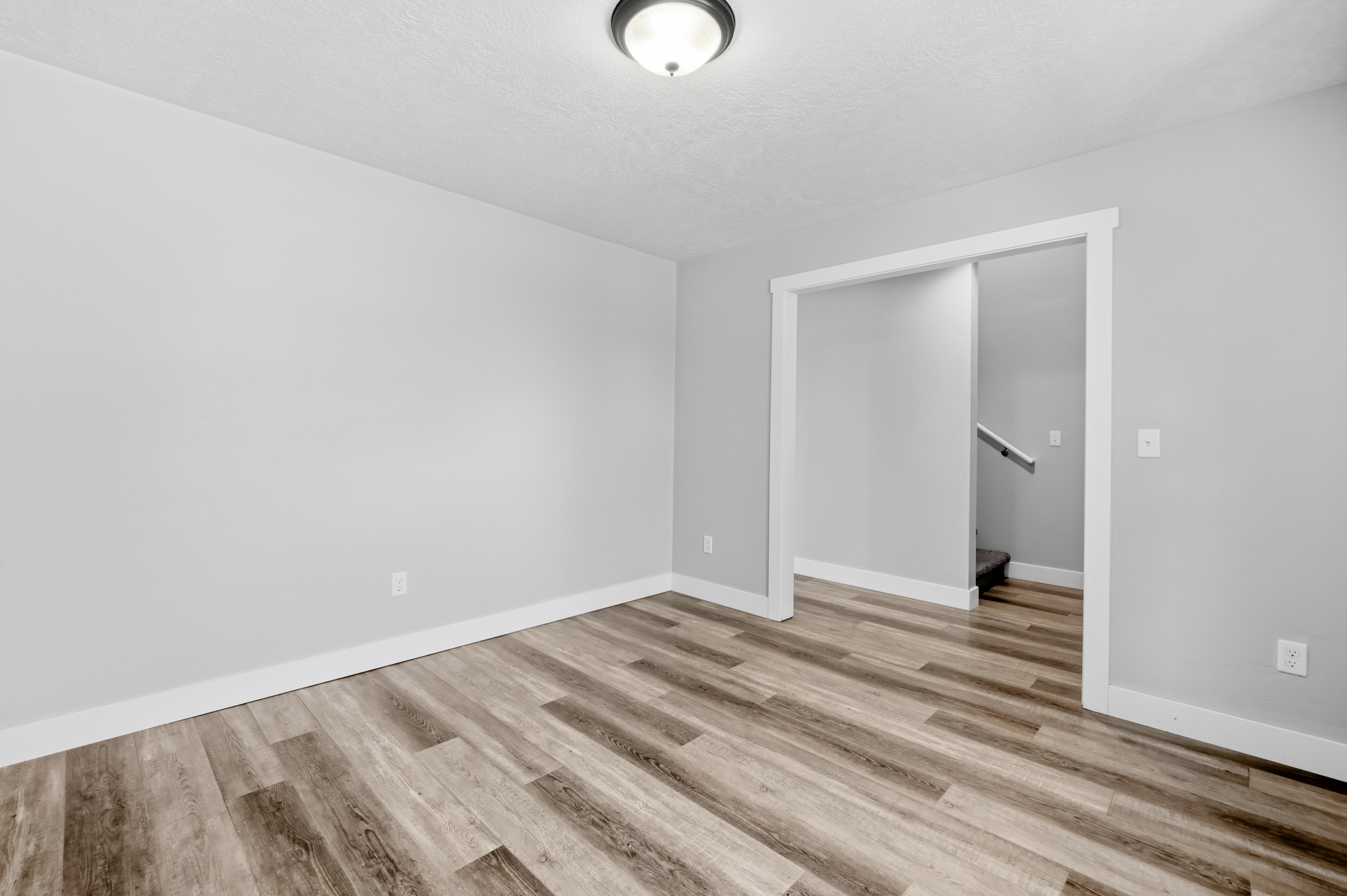 Open room featuring wood-finish flooring, light gray wall paint, white baseboards, and a semi-flush ceiling light fixture