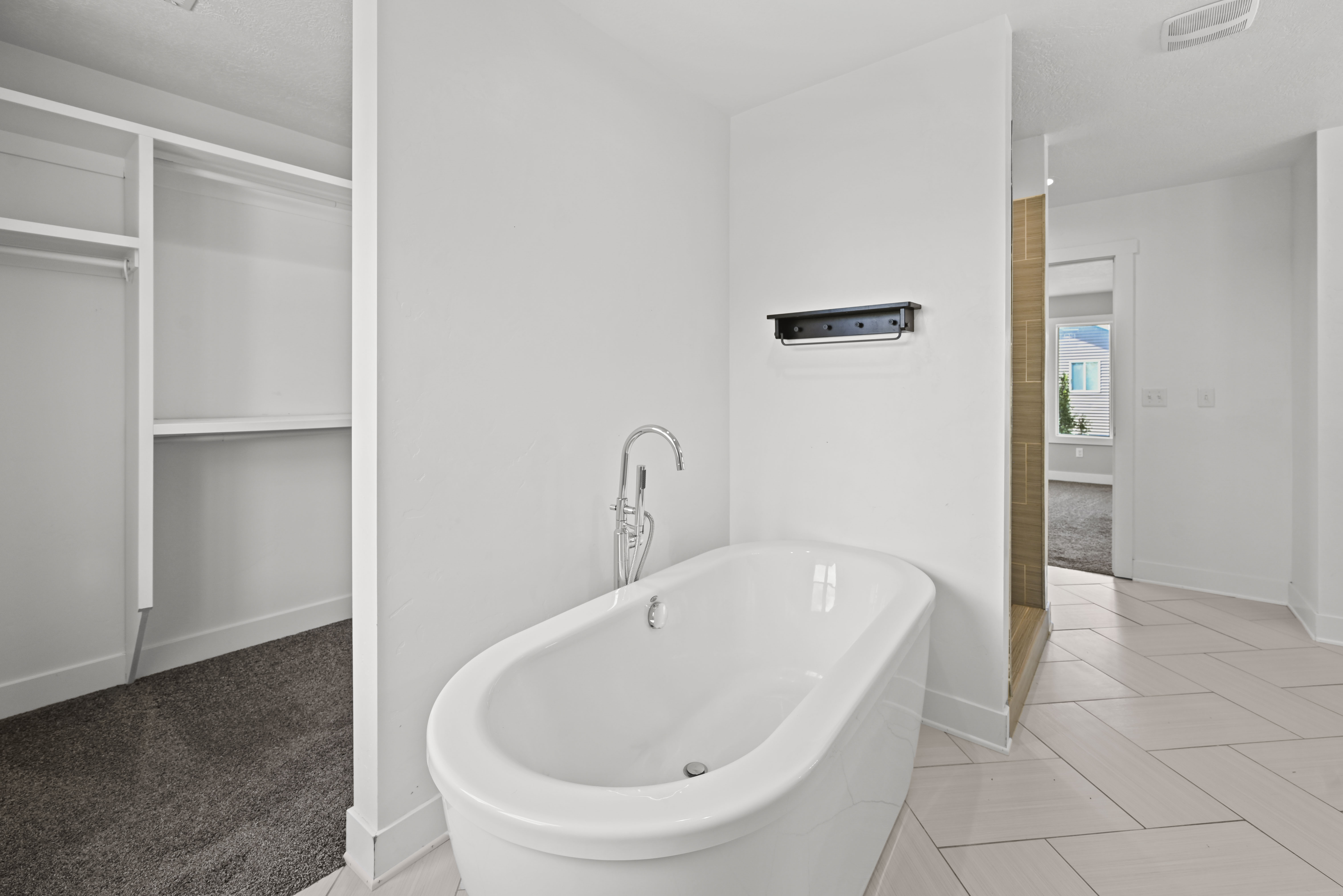Freestanding bathtub with floor-mounted faucet, herringbone tile flooring, and integrated shower stall with vertical tile detailing