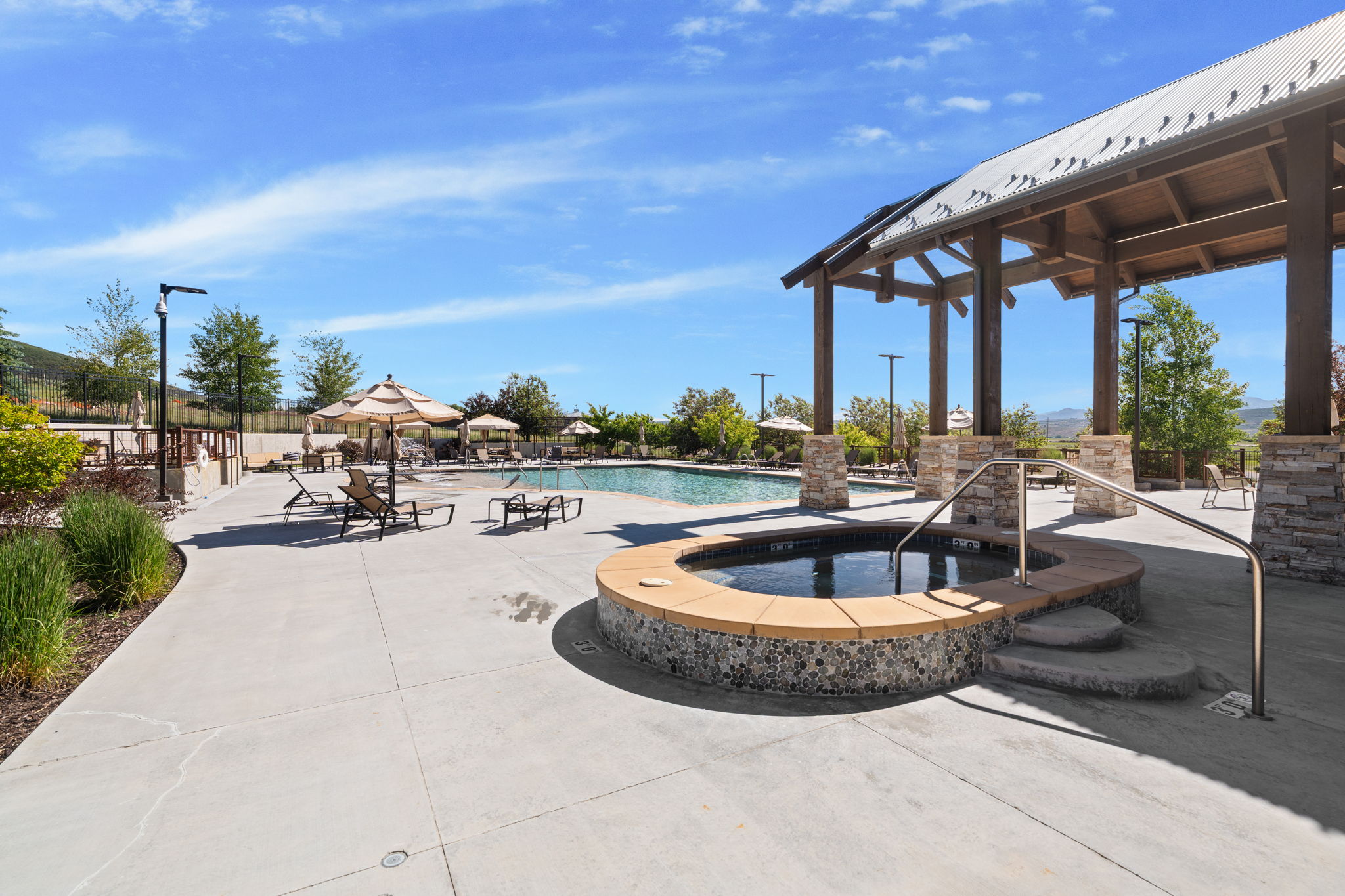 Outdoor recreation area featuring a built-in spa with mosaic tile and stone surround, a swimming pool, and an expansive concrete deck