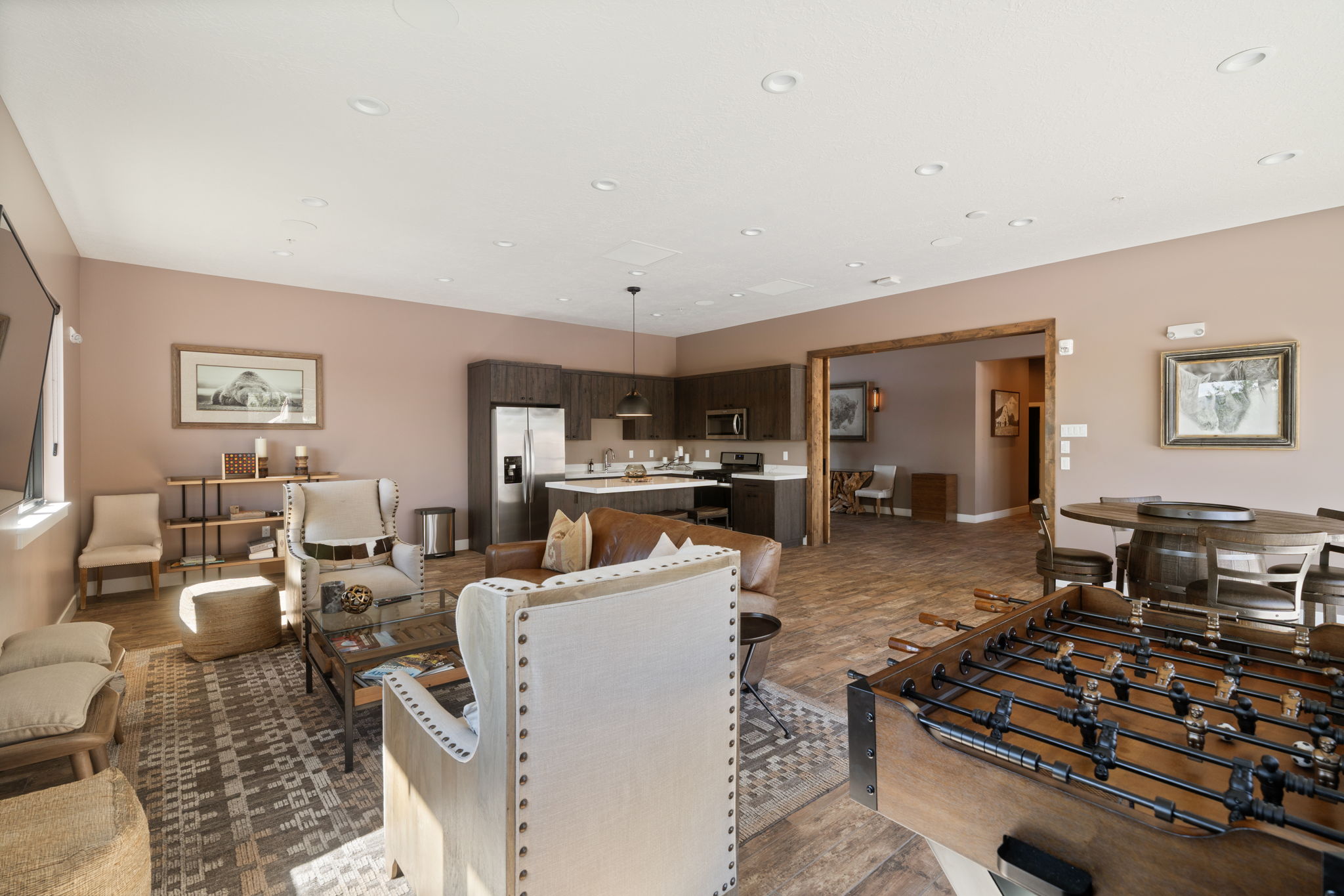 Expansive open-concept living area featuring wood-finish flooring, recessed lighting, and a modern kitchen with dark cabinetry, stainless steel appliances, and a central island