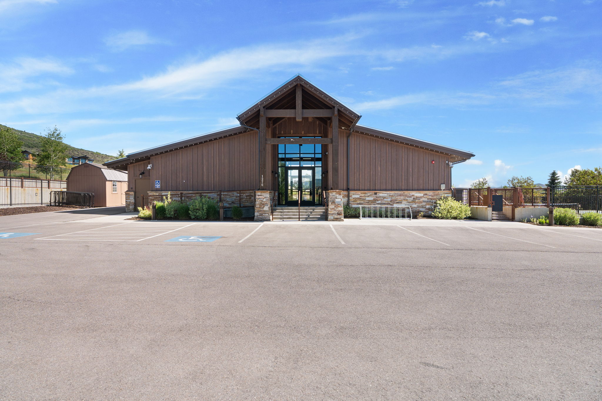 Wood-sided building with a stone-clad base, featuring an expansive parking area and a prominent gabled entrance
