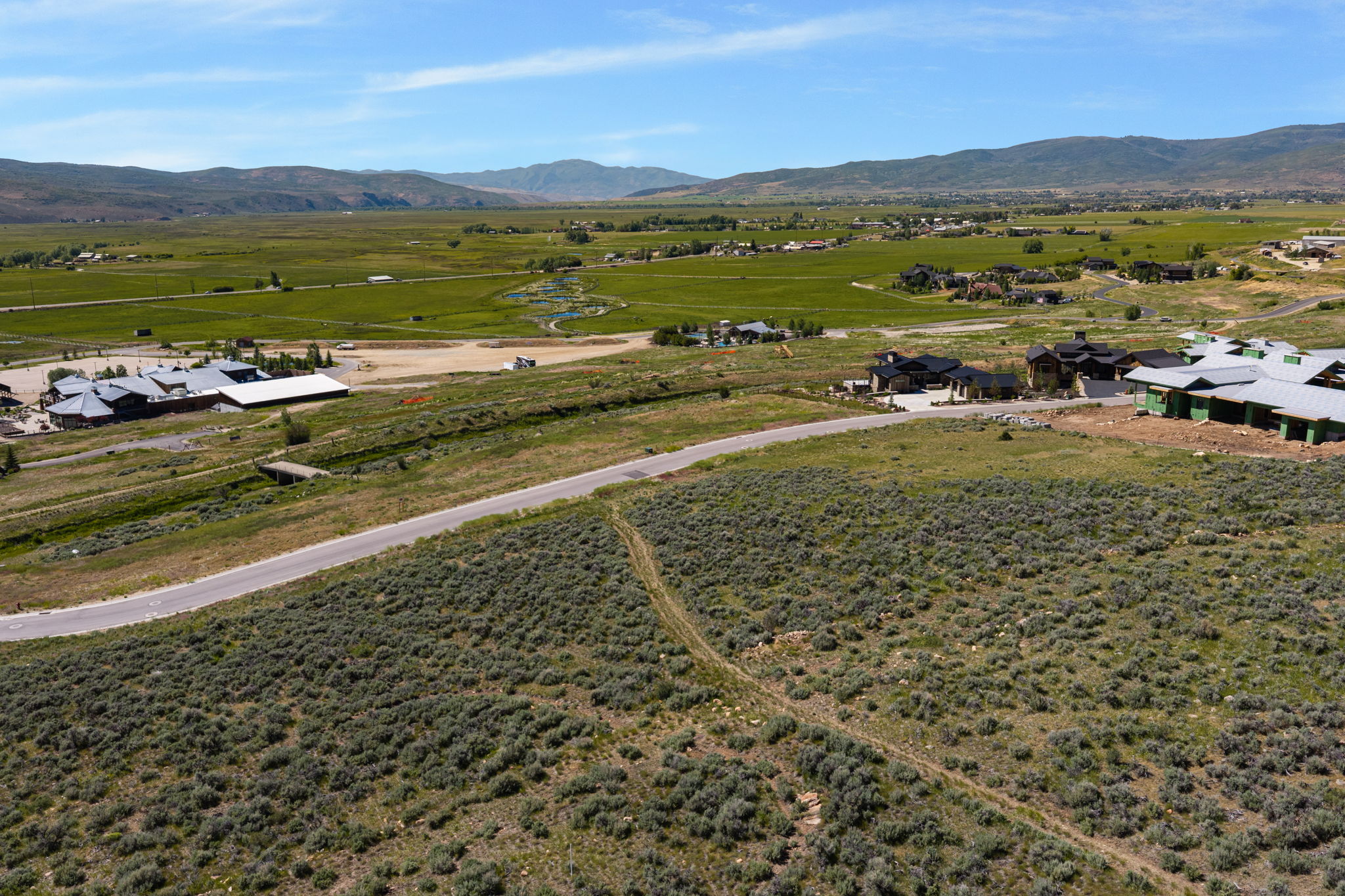 Expansive land parcel featuring natural shrubbery and a paved road, bordered by distant mountains