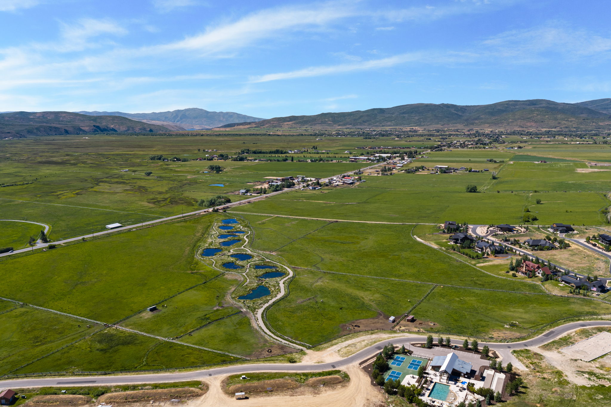 Expansive green landscape featuring multiple ponds, distant mountain ranges, and residential areas