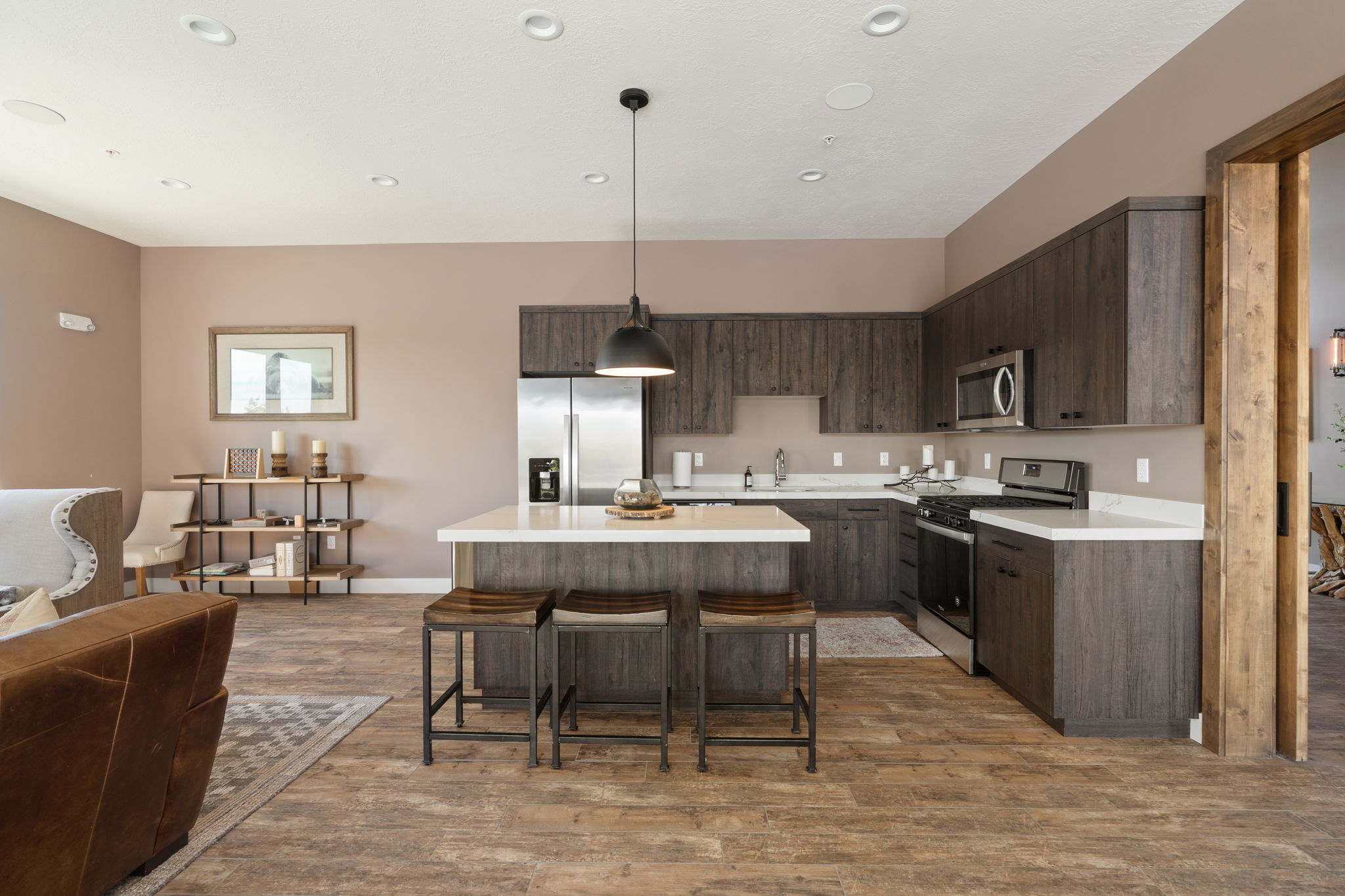 Open-concept kitchen featuring wood-finish flooring, white countertops, stainless steel appliances, and dark wood cabinetry