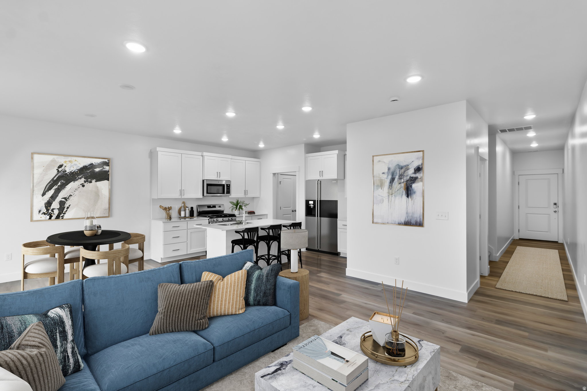 Open-concept living space featuring wood-finish flooring, recessed lighting, and a white kitchen with stainless steel appliances