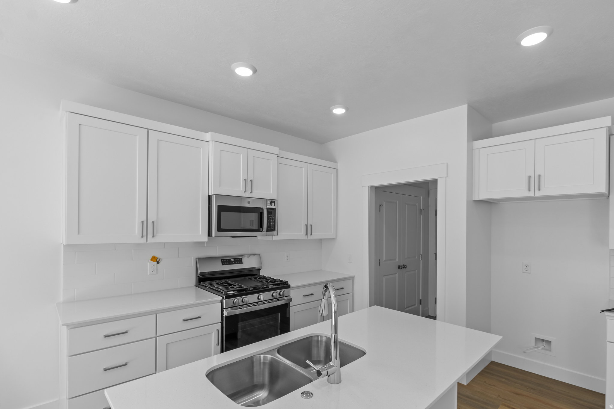 Kitchen featuring white shaker-style cabinetry, stainless steel appliances, a gas range, and an island with a dual-basin sink and a gooseneck faucet
