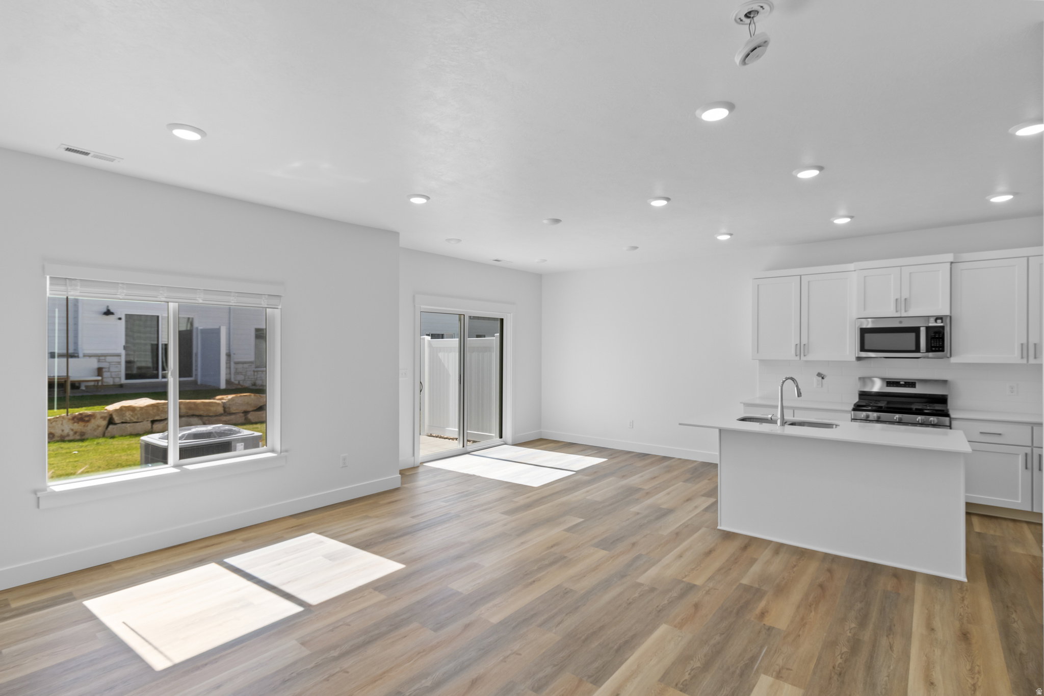Open-concept living space featuring wood-finish flooring, recessed lighting, and a white kitchen with stainless steel appliances