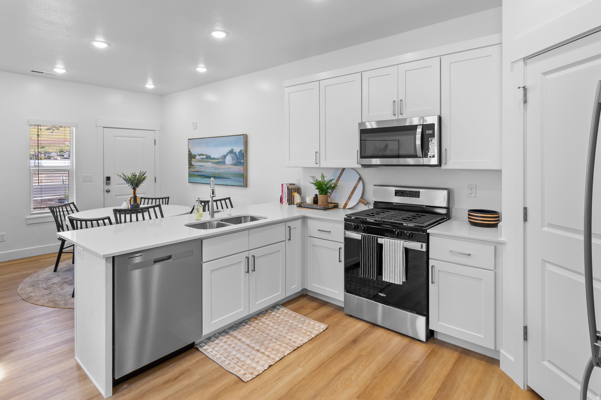 Contemporary kitchen featuring white cabinetry, stainless steel appliances, light-toned wood-finish flooring, recessed lighting, and a kitchen island with a double basin sink