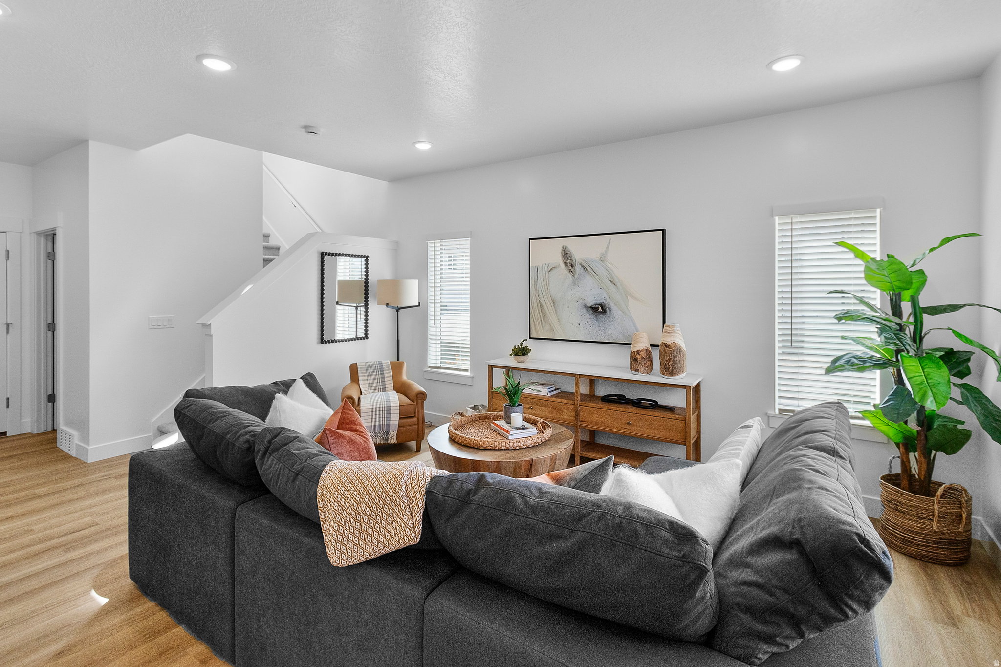 Living area featuring light wood-finish flooring, white walls, recessed lighting, and a visible staircase with white balusters