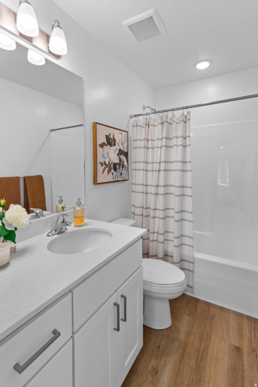 Bathroom featuring a white vanity with a light-toned countertop and an integrated sink, a full-width mirror, and wood-finish flooring