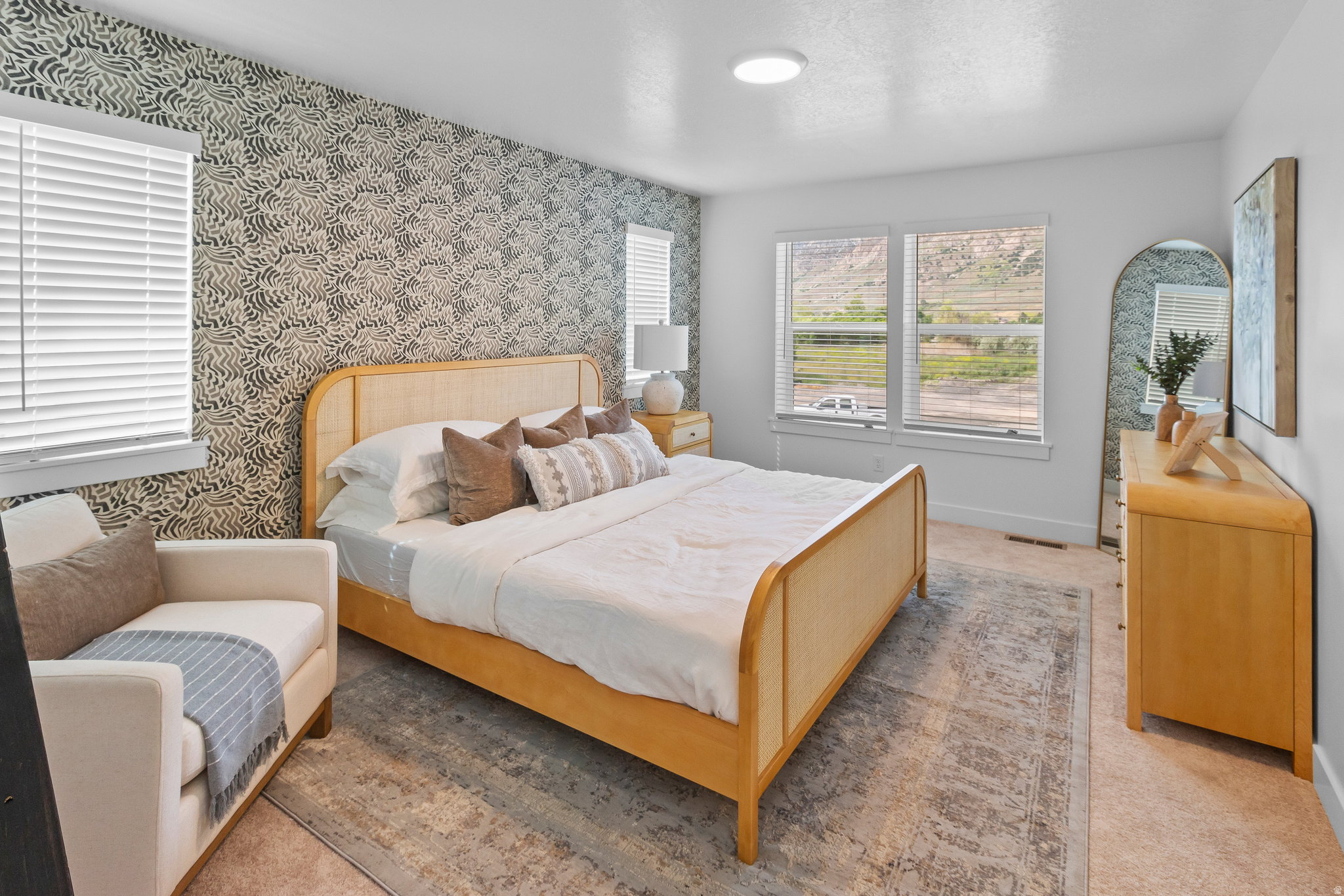 Bedroom featuring a patterned accent wall, multiple windows with blinds, a light-colored carpet, and an overhead flush-mount light fixture